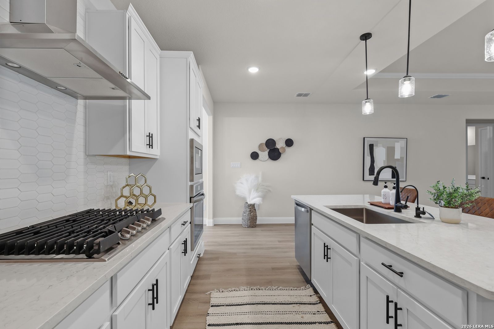 Modern white kitchen with quartz island, gas range, stainless appliances, and hexagon tile backsplash in The Lanier G by Davidson Homes, Castroville, TX