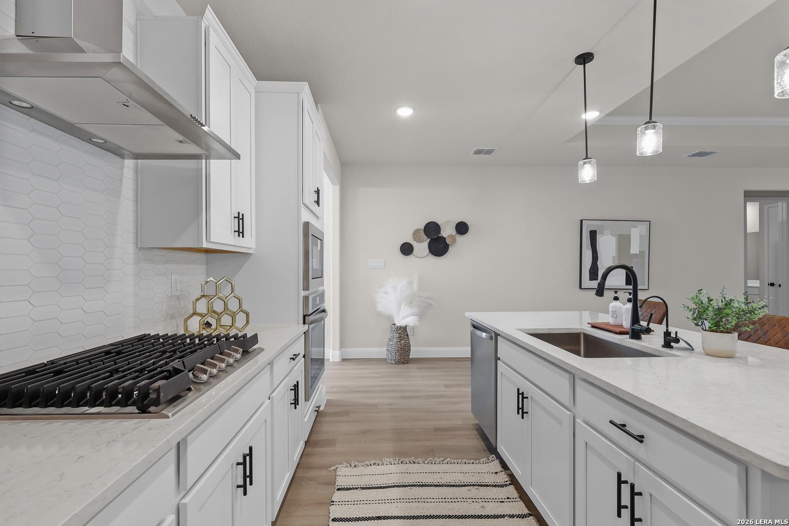 Modern white kitchen with quartz island, gas range, stainless appliances, and hexagon tile backsplash in The Lanier G by Davidson Homes, Castroville, TX