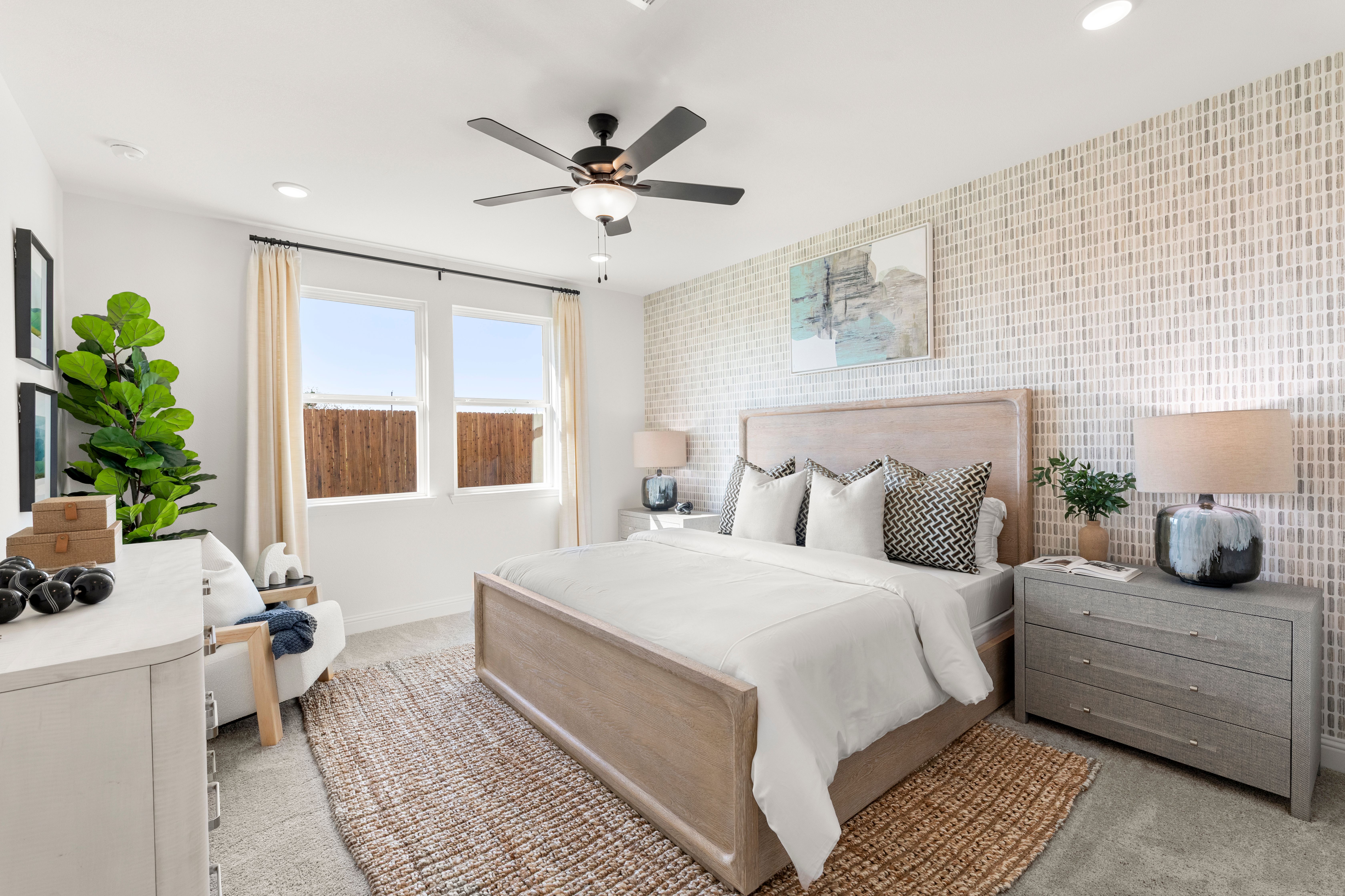 Spacious master bedroom in The Laurel I with white king bed, neutral walls, plants, ceiling fan, and large windows