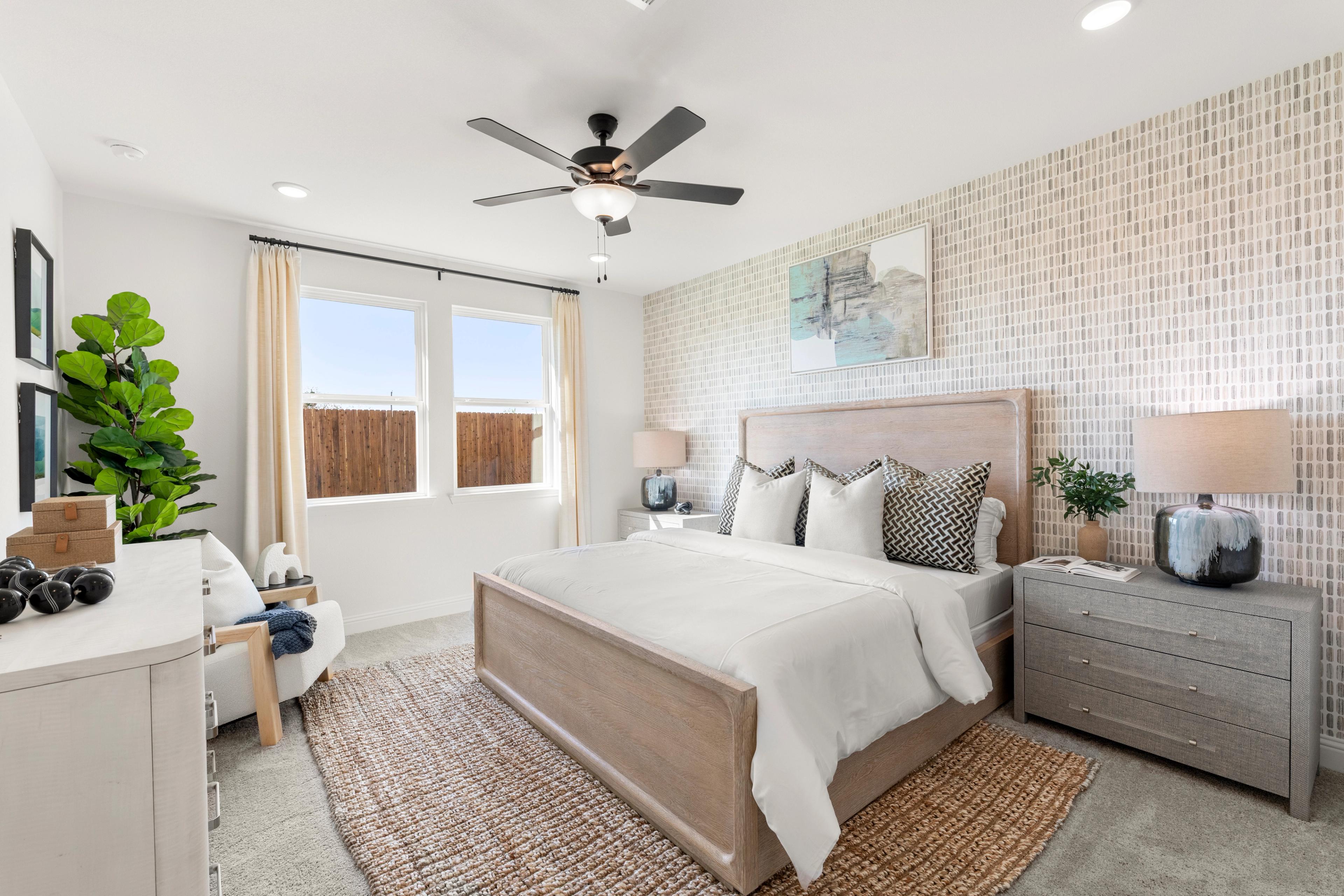 Spacious primary bedroom at Meadow Ridge Estates in Josephine Texas with king bed, neutral tones, plants, ceiling fan, and large windows