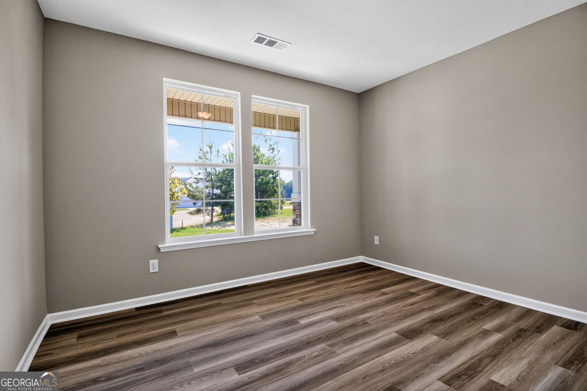 Bright secondary bedroom with gray walls, large windows, and wood-look flooring in The Luna home by Evermore Homes, Perry, Georgia