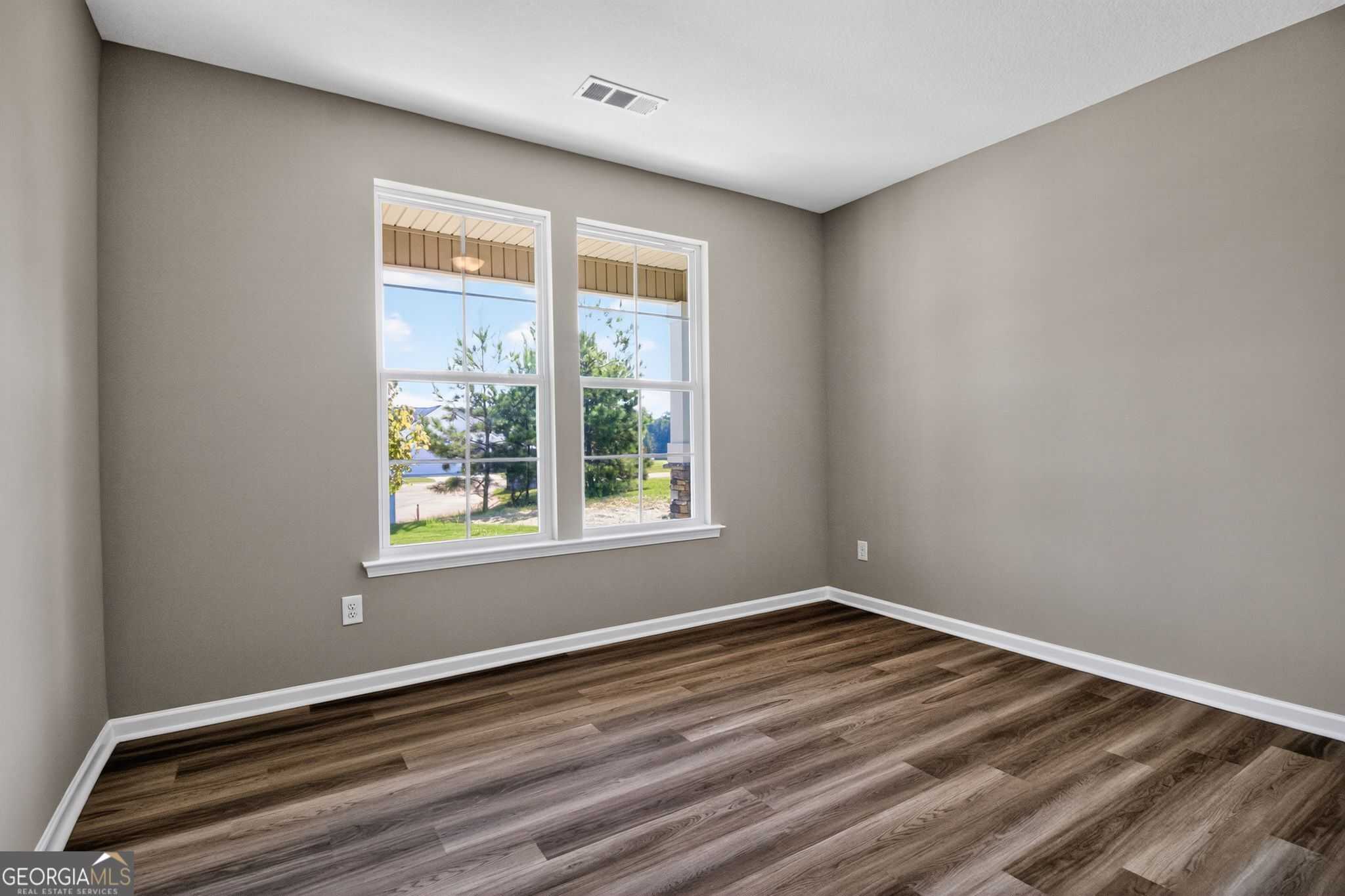 Bright bedroom with gray walls, large sunny windows overlooking trees, and wood-look flooring in Evermore Homes The Luna, Perry, GA