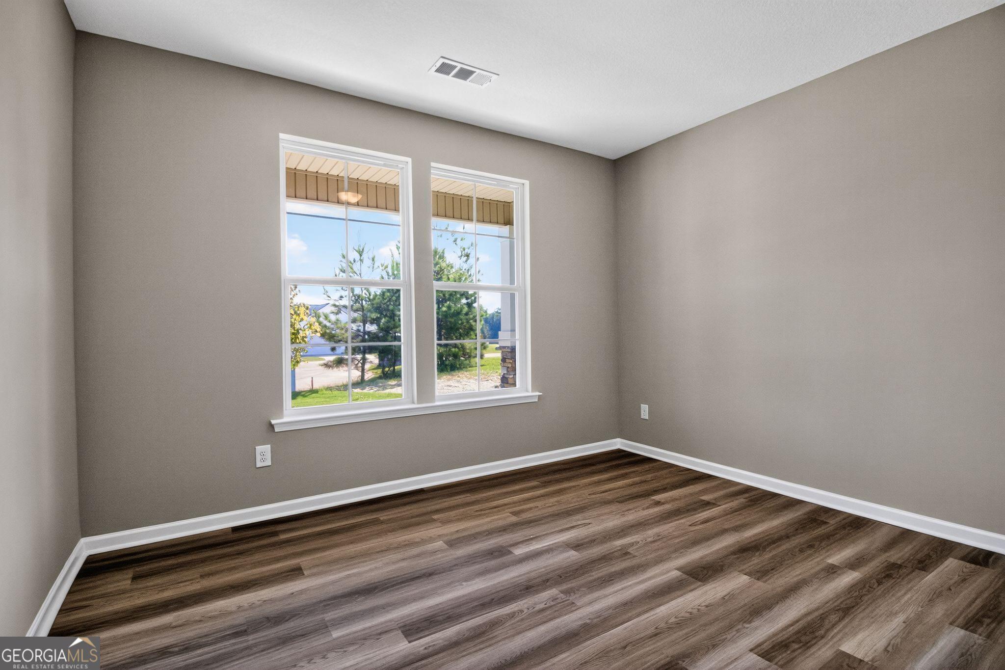 Bright secondary bedroom with gray walls, large windows, and wood-look flooring in The Luna home by Evermore Homes, Perry, Georgia