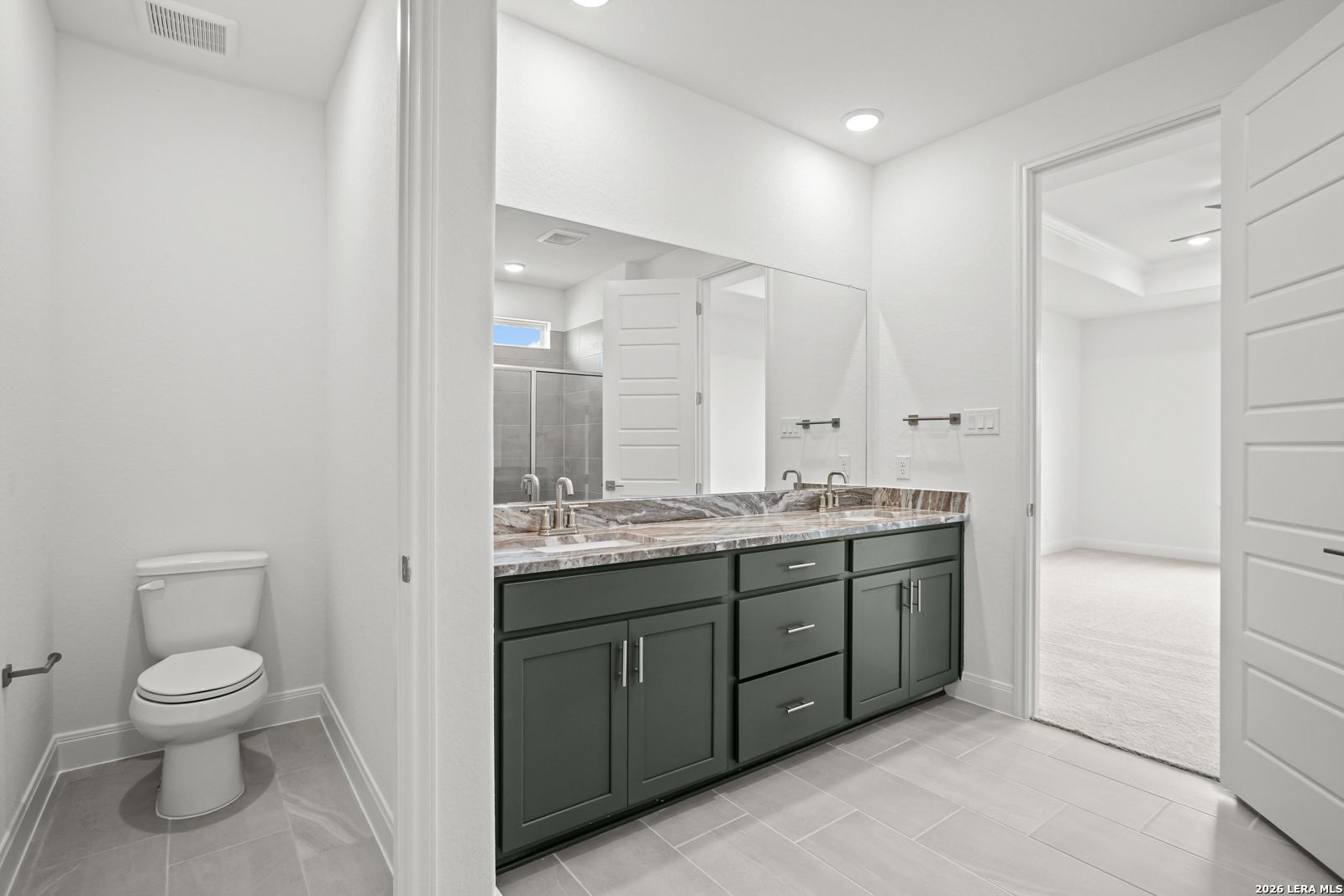 Modern ensuite bathroom with dual-sink vanity and dark green cabinetry in The Lanier G floor plan, Castroville, Texas.