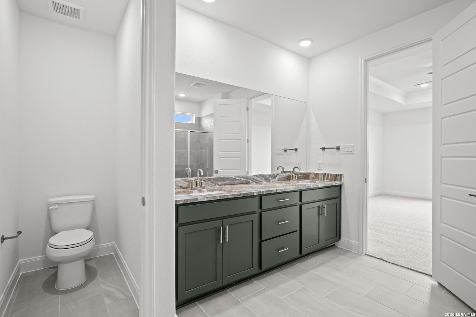 Modern ensuite bathroom with dual-sink vanity and dark green cabinetry in The Lanier G floor plan, Castroville, Texas.