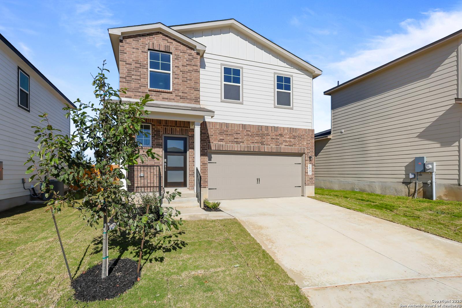 Modern two-story brick home with white siding, 2-car garage, front porch, and young tree in green yard, Applewhite Meadows, San Antonio