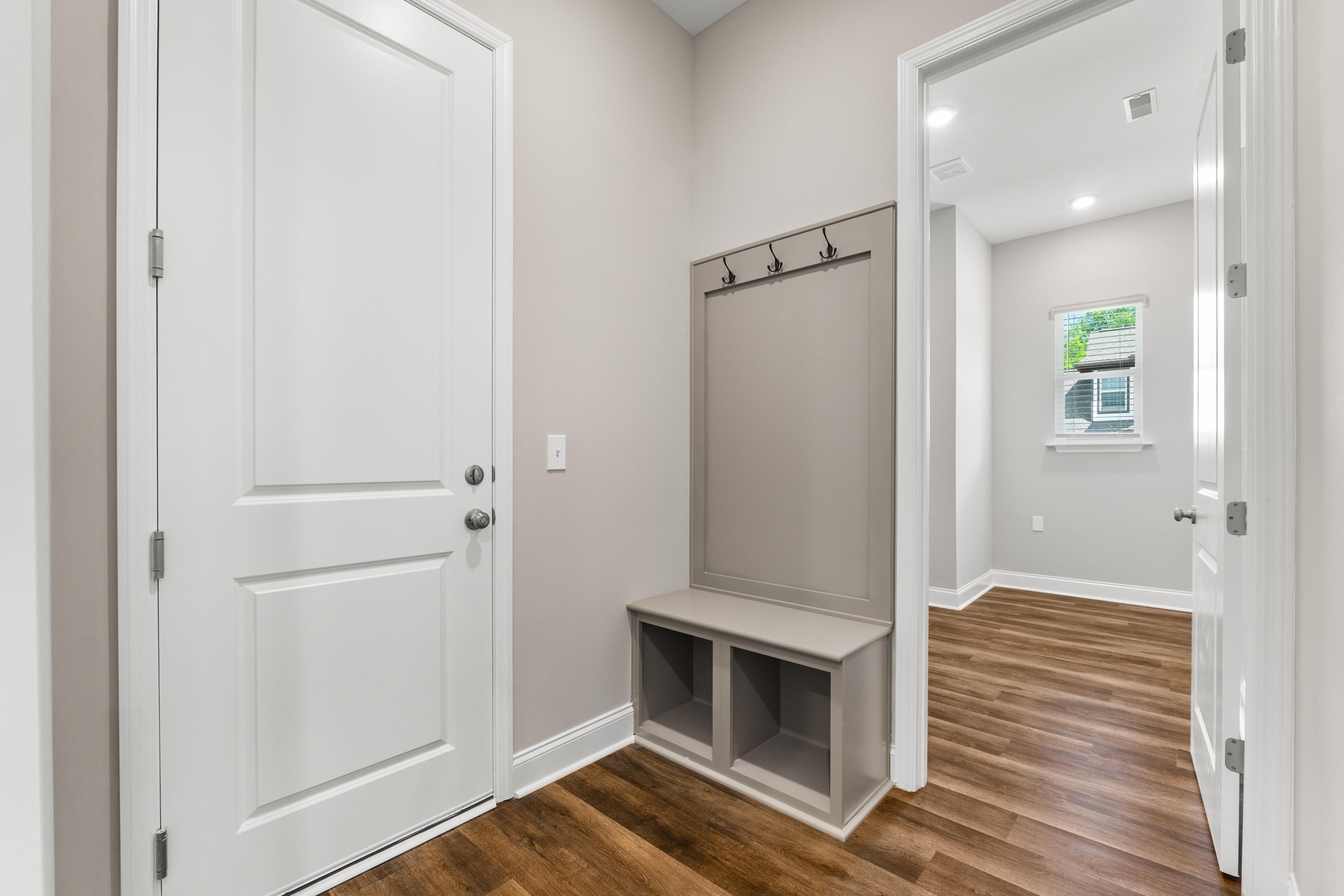 Spacious mudroom in The Arcadia B with gray bench, coat hooks, white doors, and wood floors
