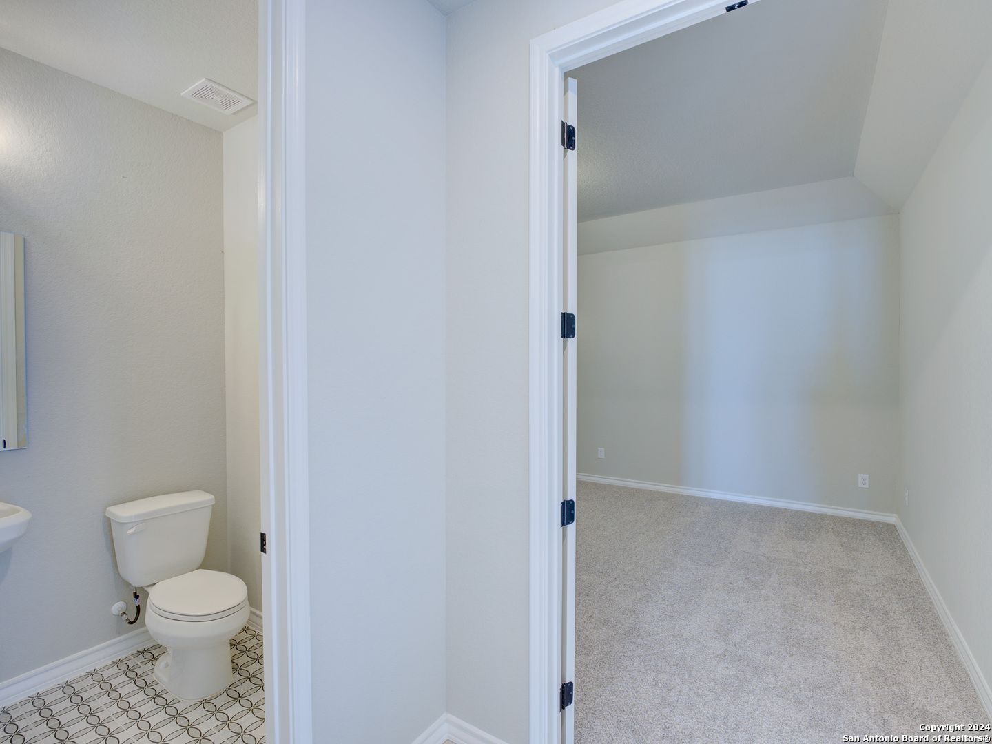 Elegant half bath with white pedestal sink, toilet, and subway tile floor adjacent to carpeted bedroom in Davidson Homes Summerlin A, Castroville, Texas