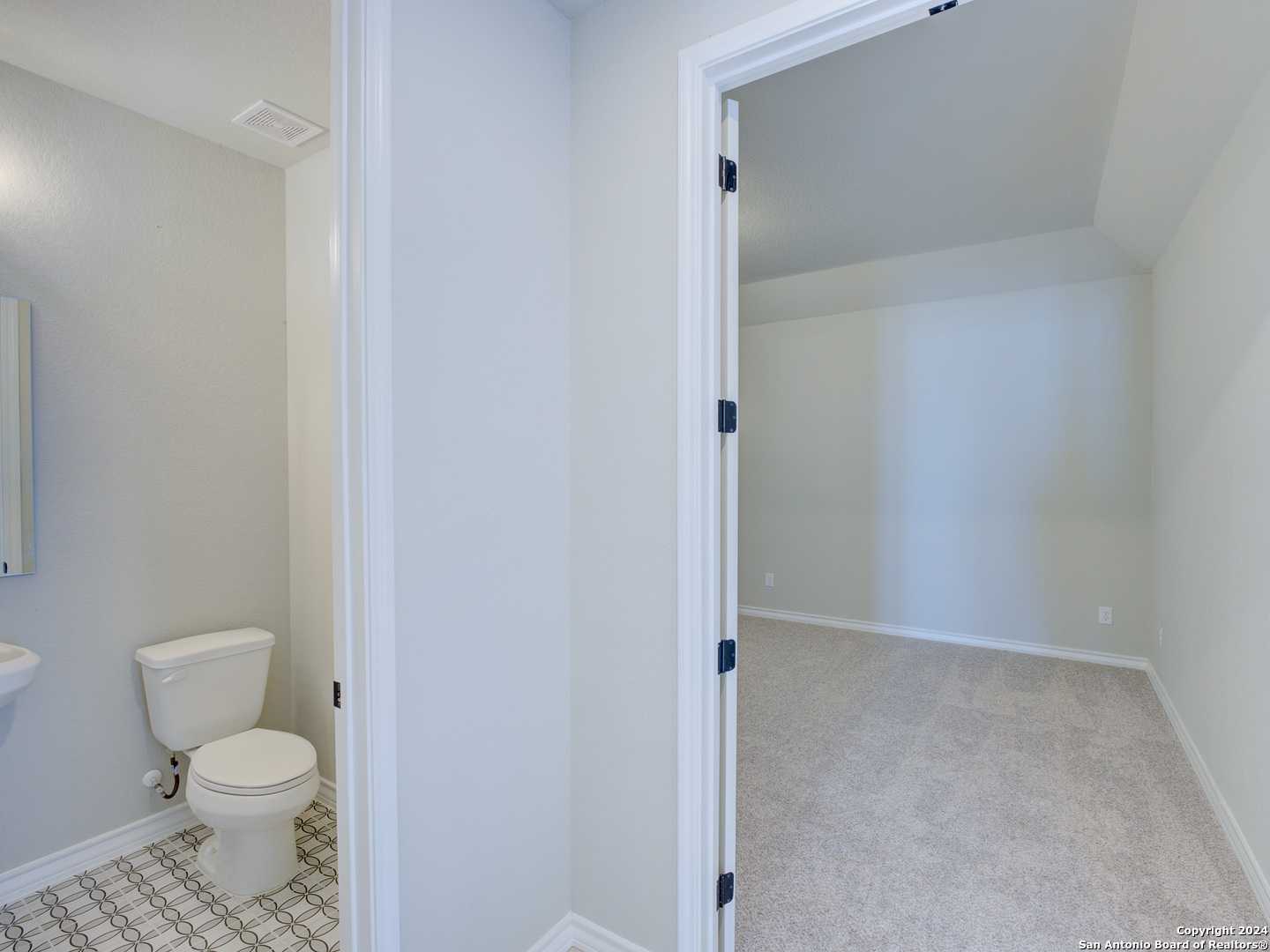 Elegant half bath with white pedestal sink, toilet, and subway tile floor adjacent to carpeted bedroom in Davidson Homes Summerlin A, Castroville, Texas
