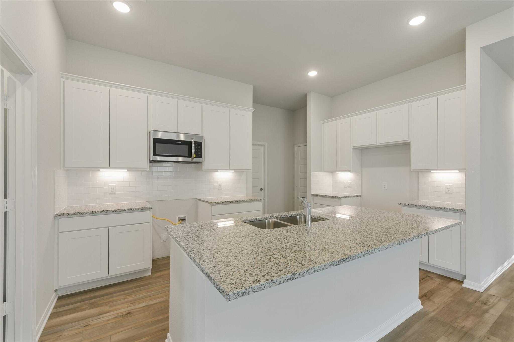 Modern white kitchen with granite island, stainless microwave, and recessed lights in Davidson Homes The Laguna B, Dayton, Texas
