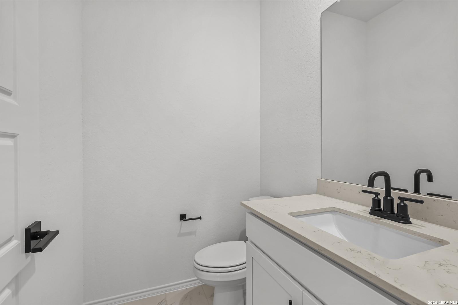 Modern half bath with white vanity, stone countertop, and matte black fixtures in The Gillian C home, San Antonio, Texas.