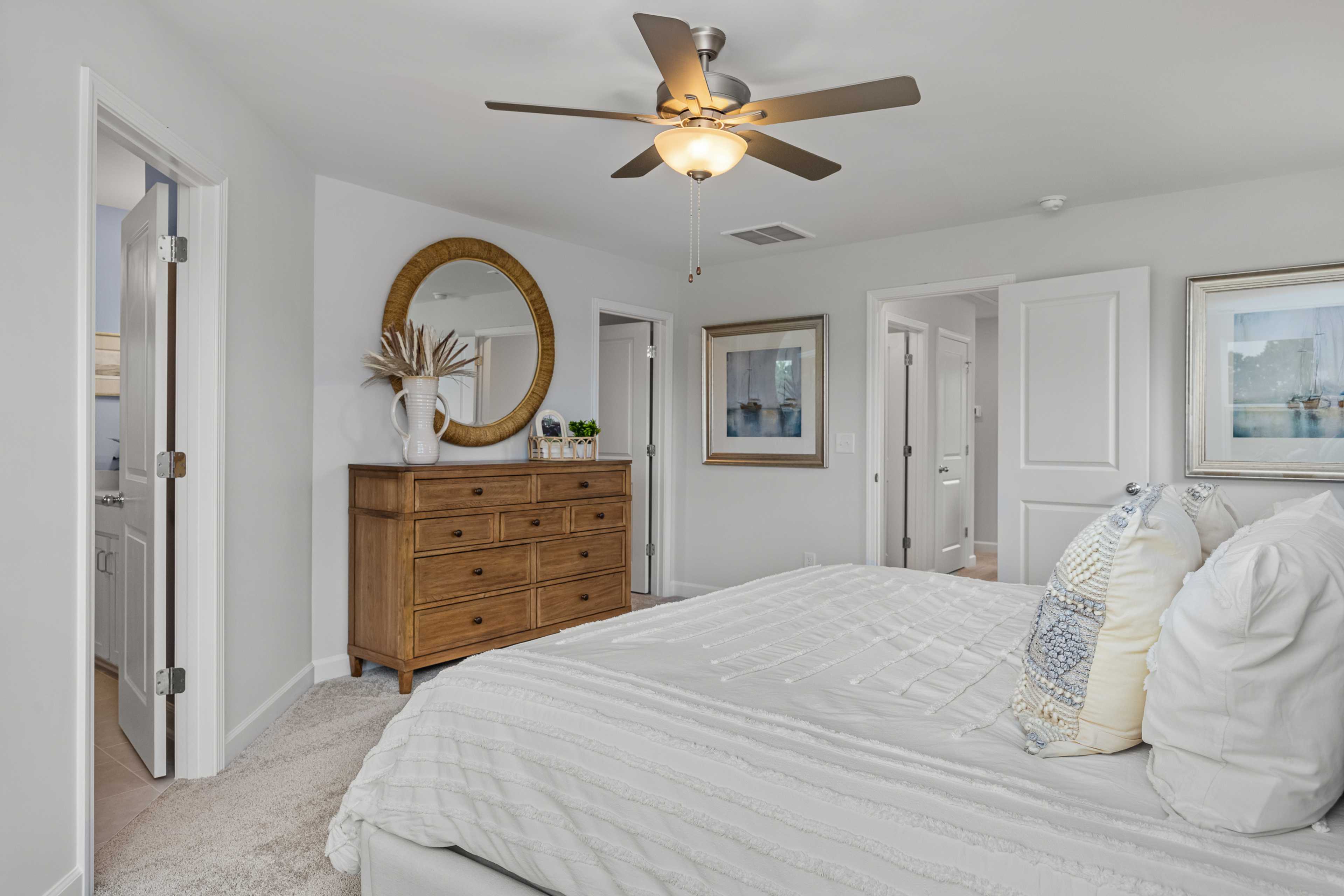 Spacious primary bedroom at Springvale in Fuquay-Varina NC with white tufted bed, wooden dresser, gold mirror, ceiling fan
