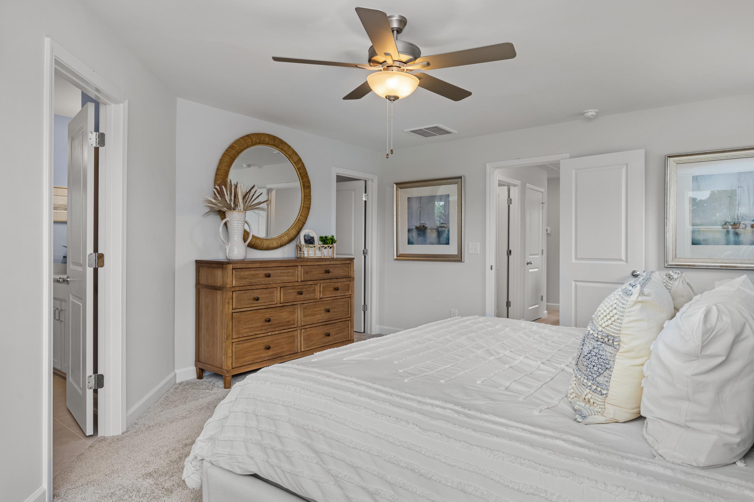 Spacious primary bedroom at Springvale in Fuquay-Varina NC with white tufted bed, wooden dresser, gold mirror, ceiling fan