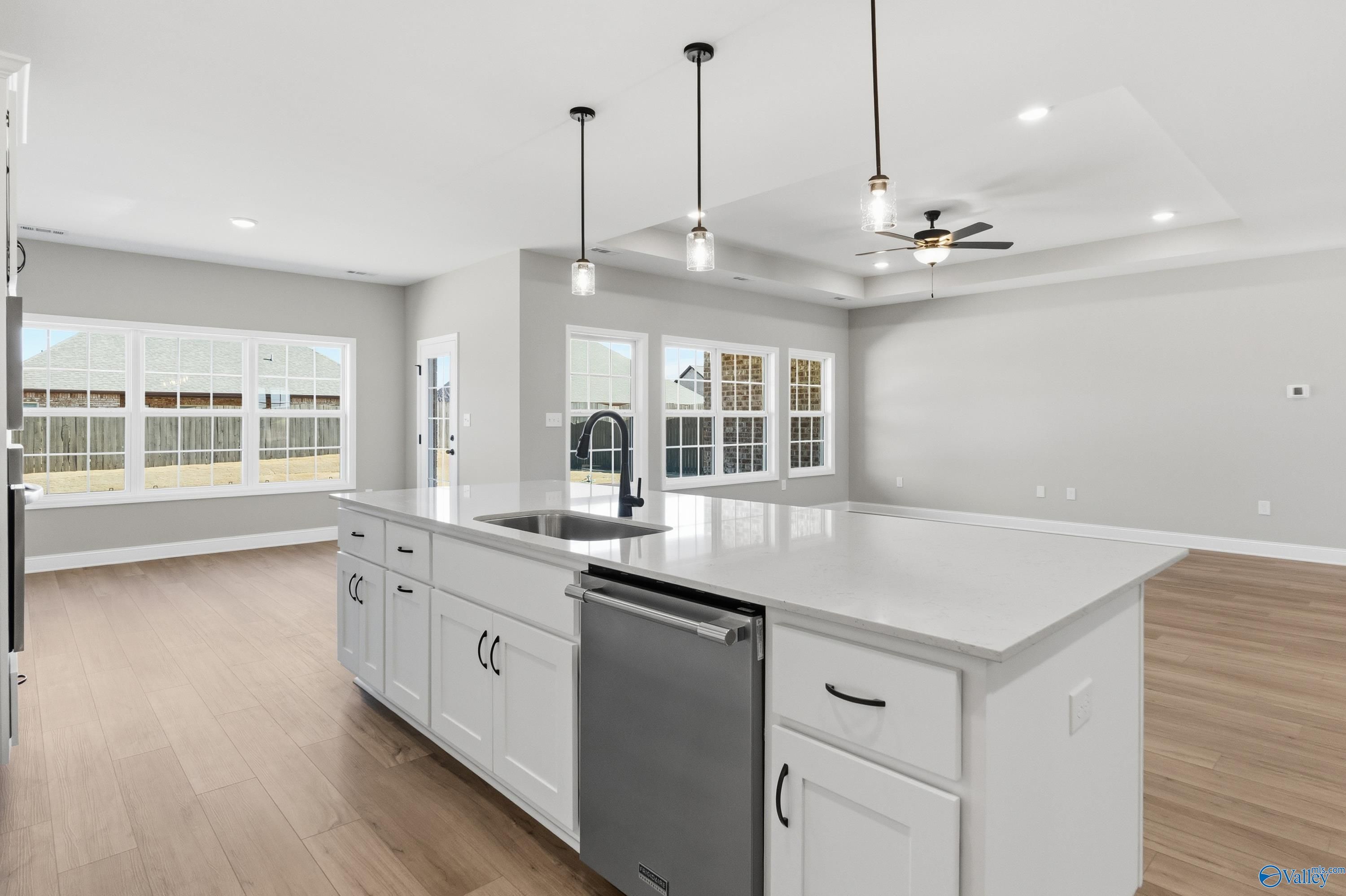 Modern open-concept kitchen with white quartz island, stainless dishwasher, pendant lights, and wood floors in The Finleigh by Davidson Homes, Meridianville, AL