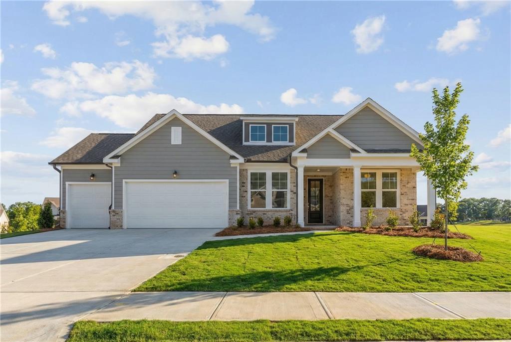Modern gray craftsman-style single-story home with 3-car garage, brick accents, and front porch in Wehunt Meadows, Hoschton, Georgia