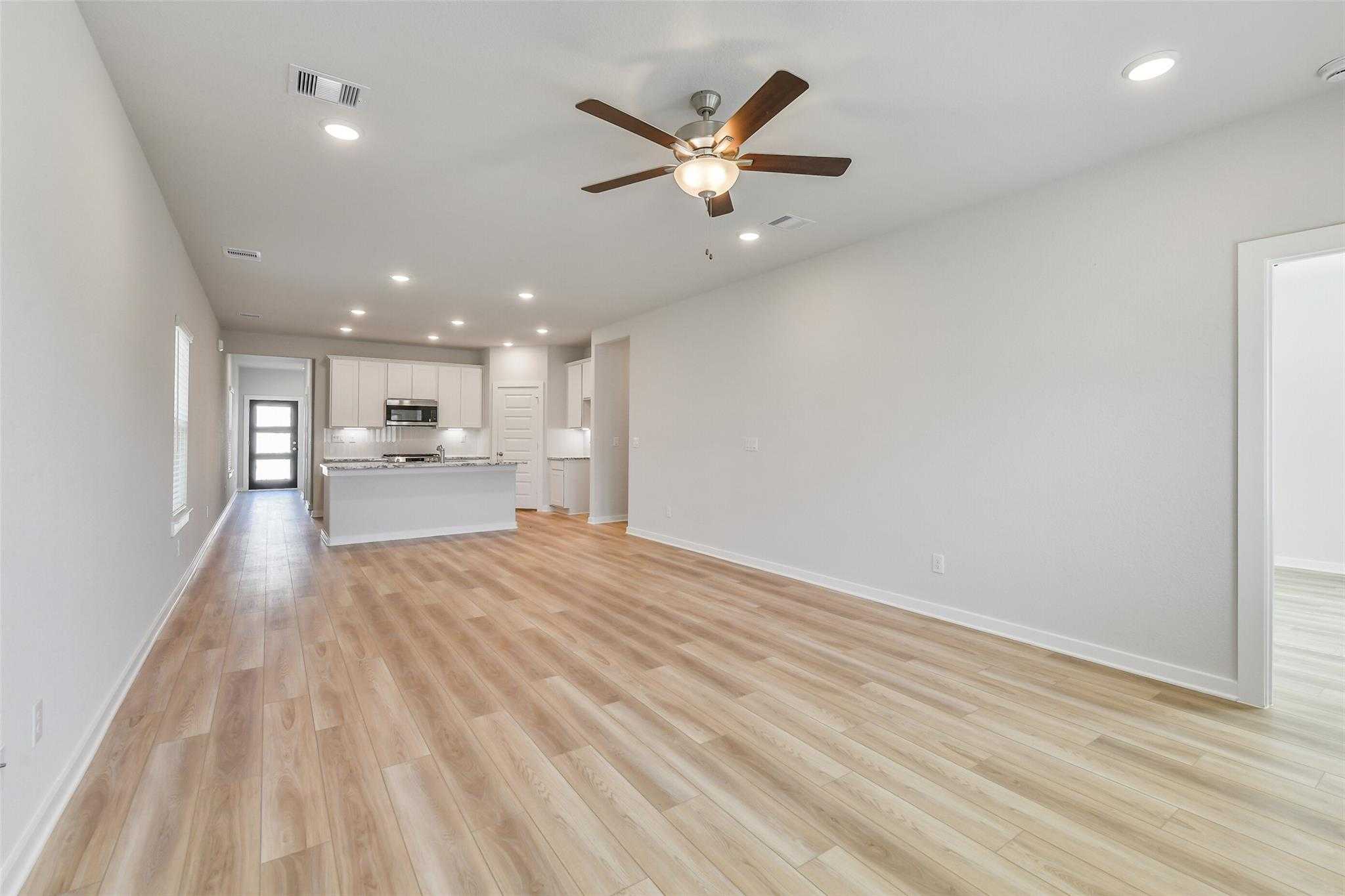 Open-concept living and kitchen area with hardwood floors, white cabinetry, and ceiling fans in Davidson Homes The Rio Grande H, Magnolia, Texas