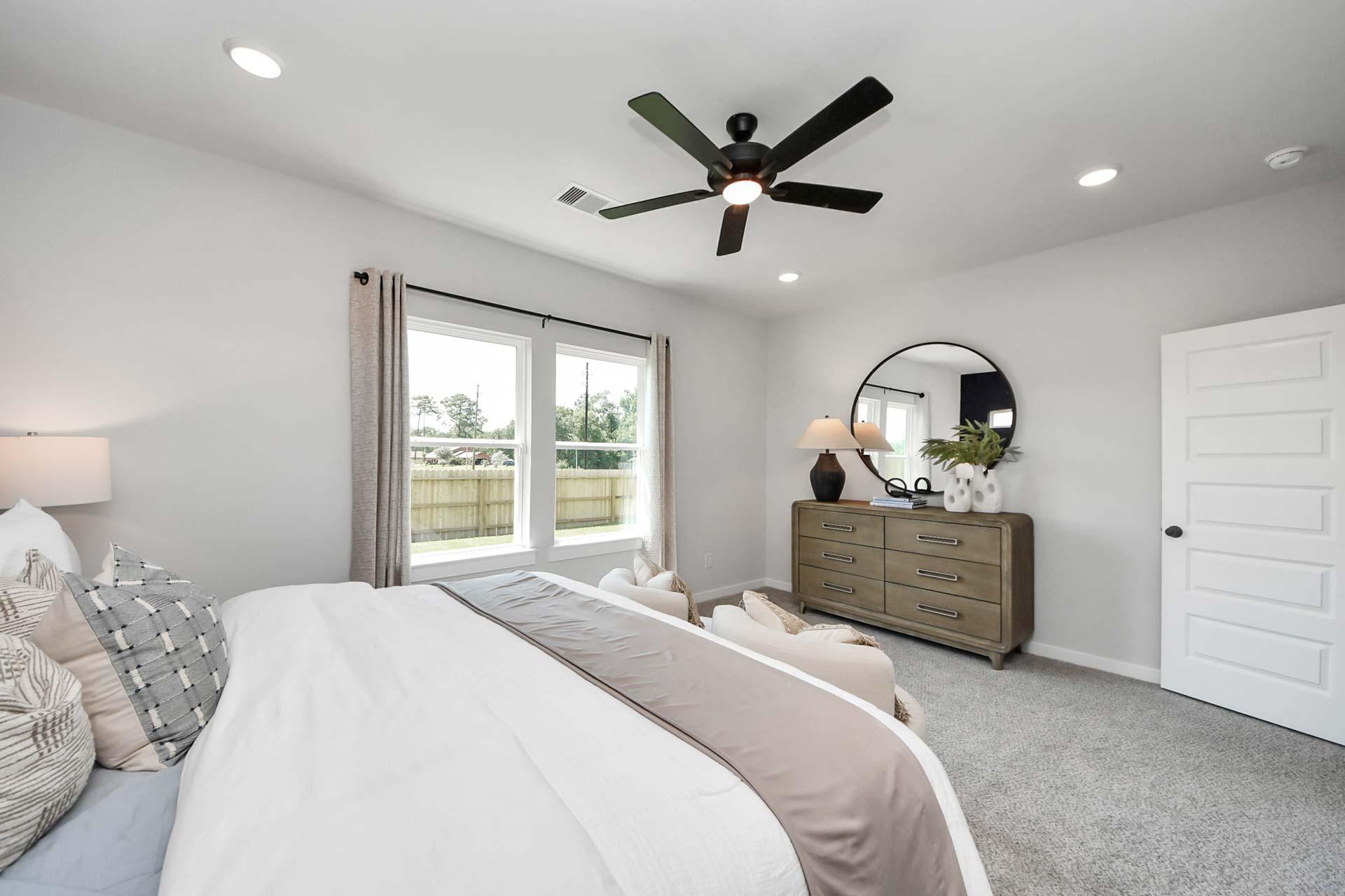 Spacious primary bedroom at Enclave at Newport in Crosby, TX by Davidson Homes featuring a modern dresser and ceiling fan.