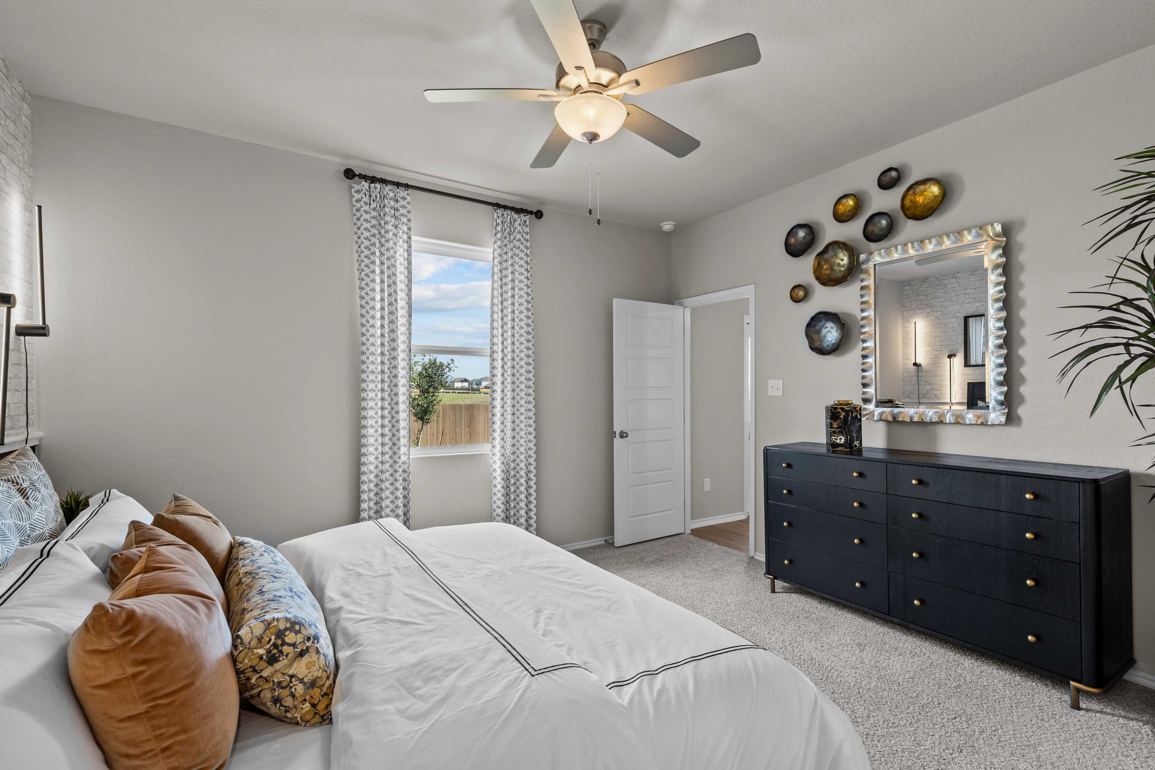 Master bedroom in The Sabine C showcasing king bed with neutral linens, black dresser, ceiling fan, and window view