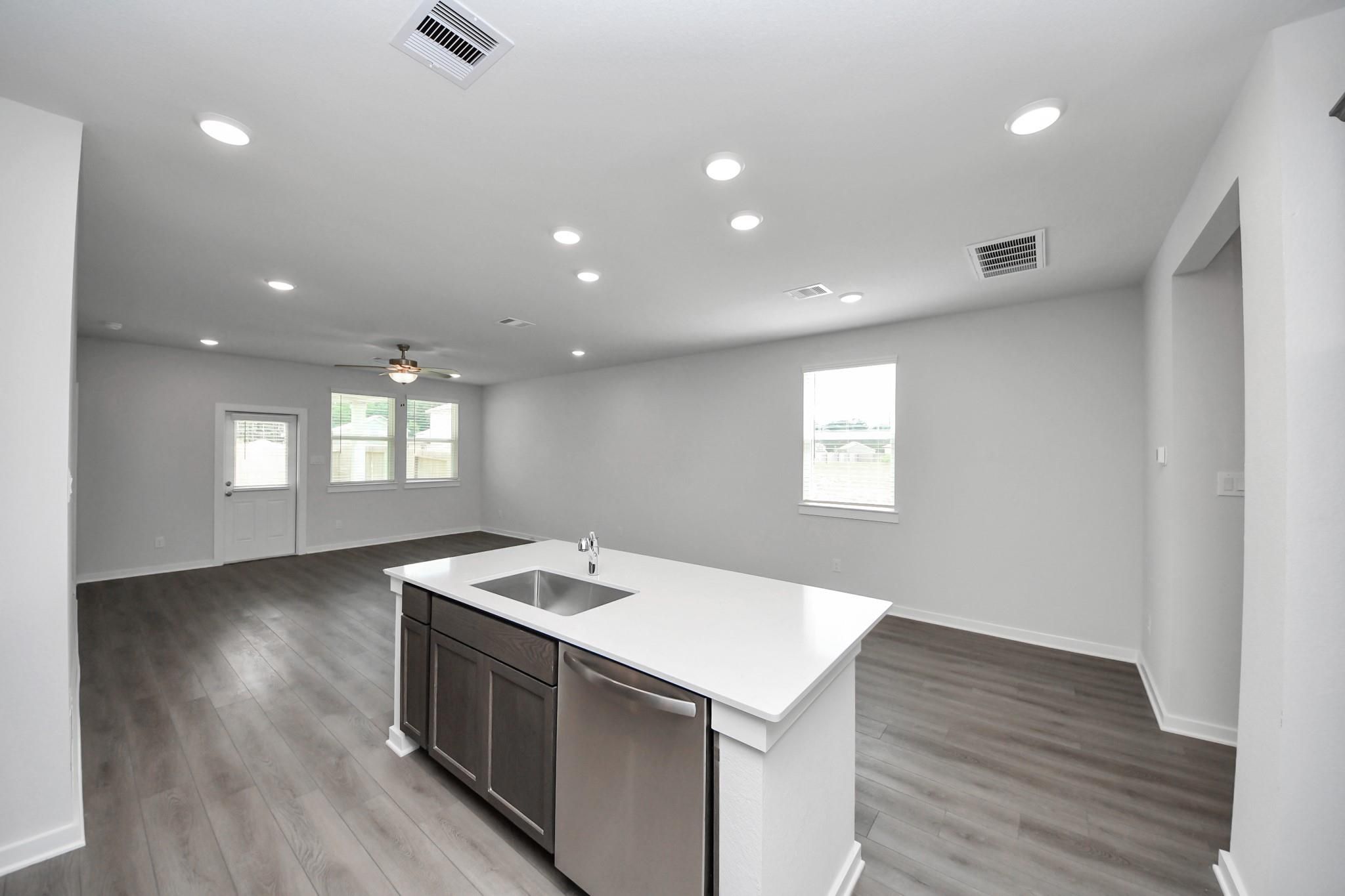 Open-concept kitchen with island and wood-look flooring in The Brazos F floor plan, Liberty Estates, Cleveland, Texas.