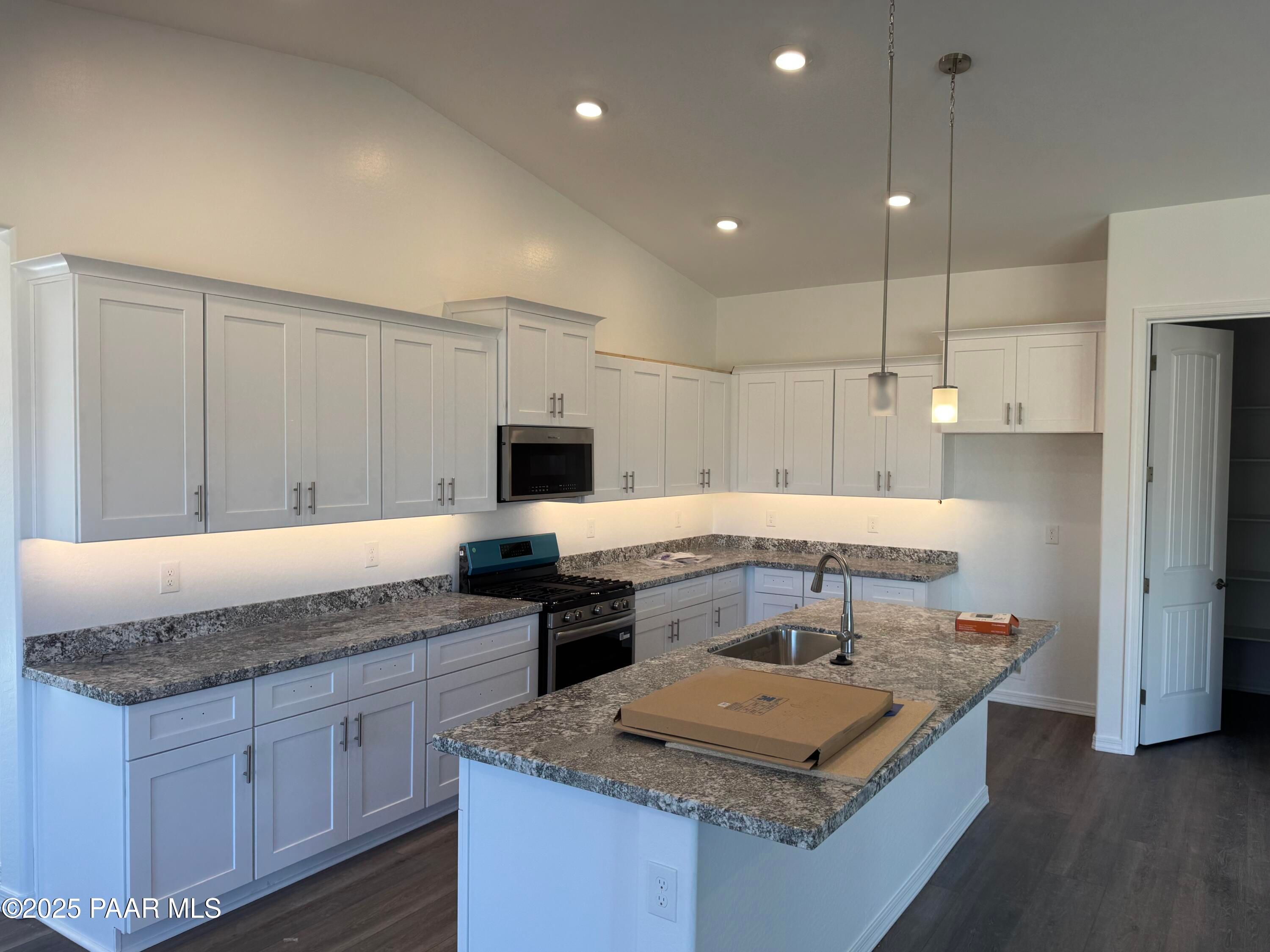 Modern white shaker kitchen with granite island, stainless gas range, pendant lights in Davidson Homes Sunrise II A, Prescott AZ