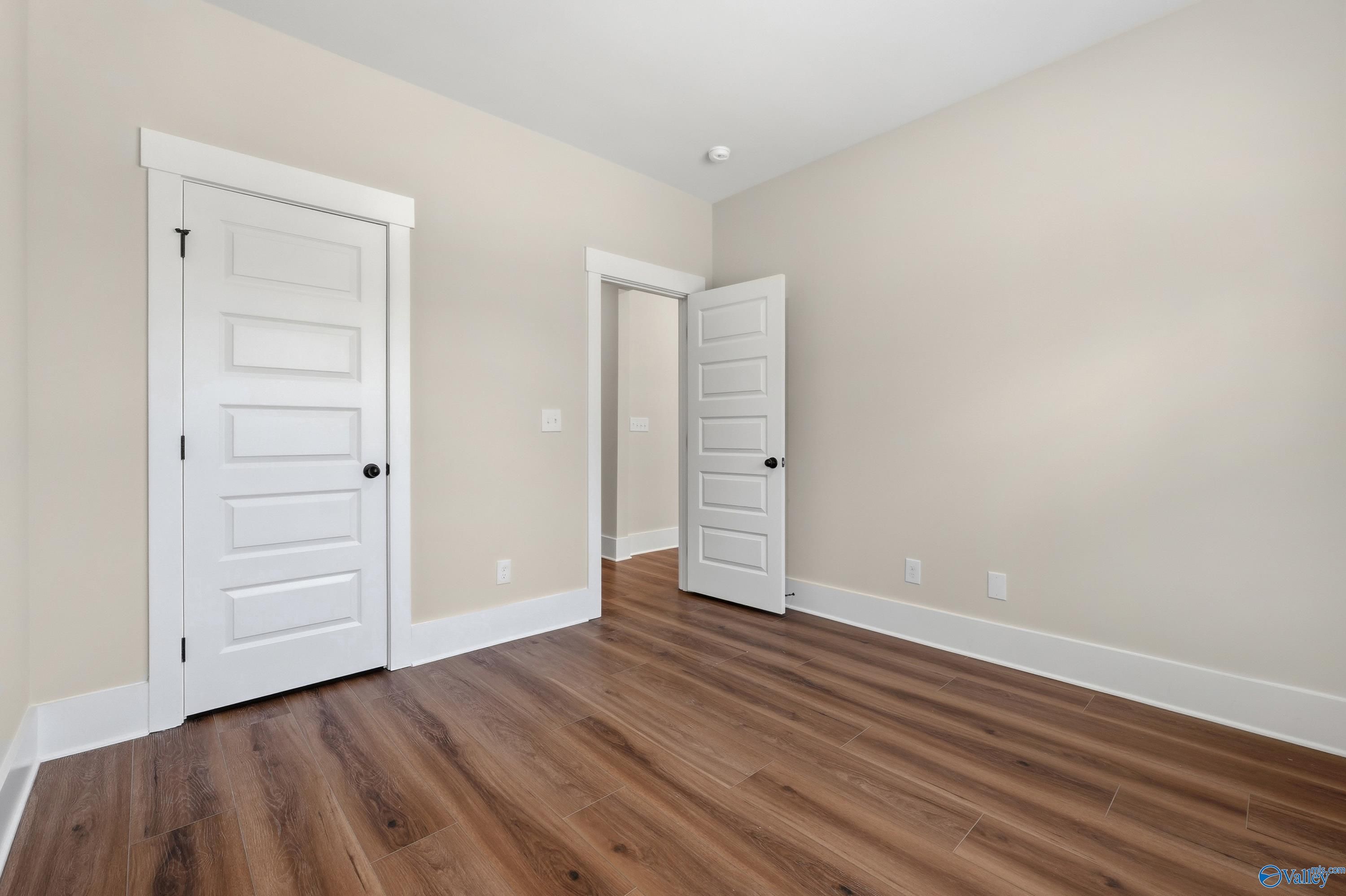 Empty bedroom with beige walls, warm hardwood floors, and open paneled doors in Davidson Homes The Shelby A, Athens, Alabama