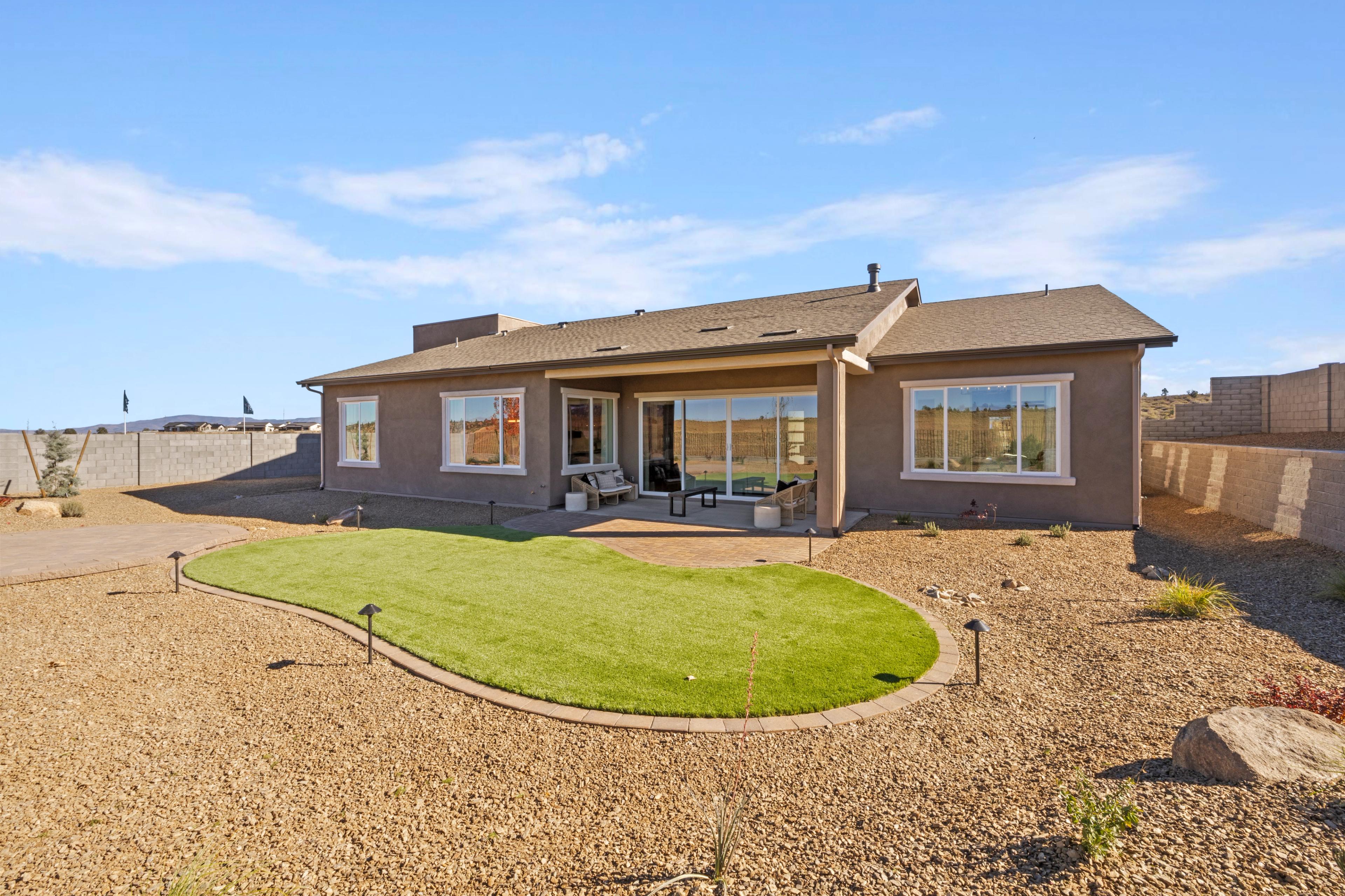 Tan stucco home backyard at Hidden Hills in Prescott Arizona with curved putting green, patio seating, and desert landscaping