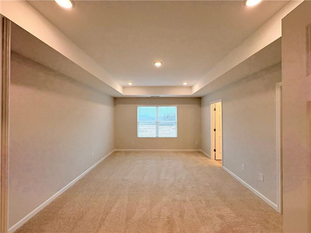 Bright master bedroom with tray ceiling, large window, recessed lights, and beige carpet in The Wake E, Cumming, GA