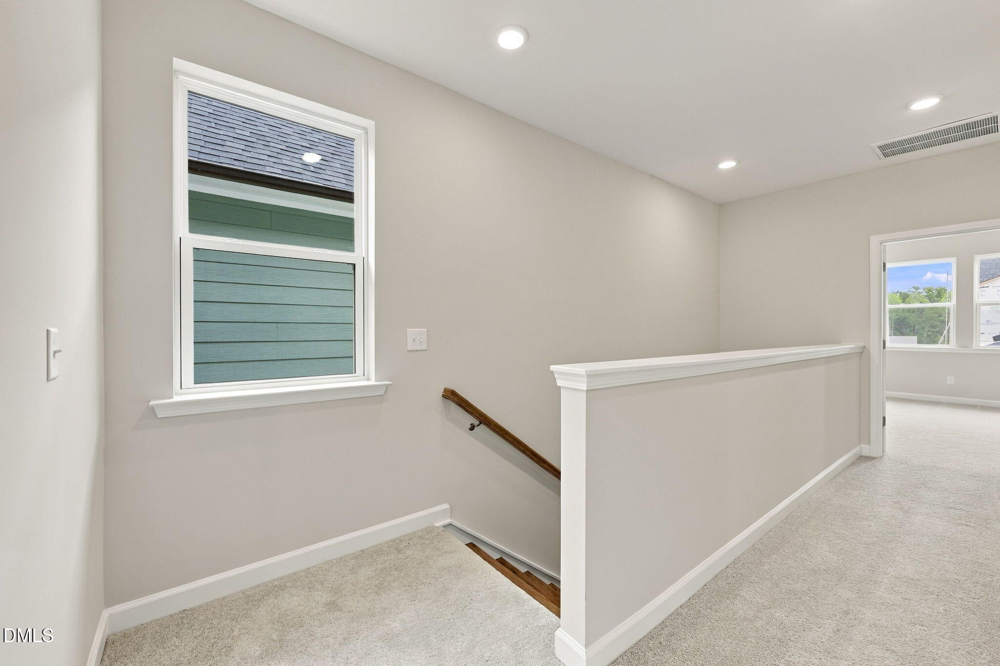 Bright upstairs loft hallway with carpet, wood stair handrail, and window in Davidson Homes The Alexander B, Knightdale, NC
