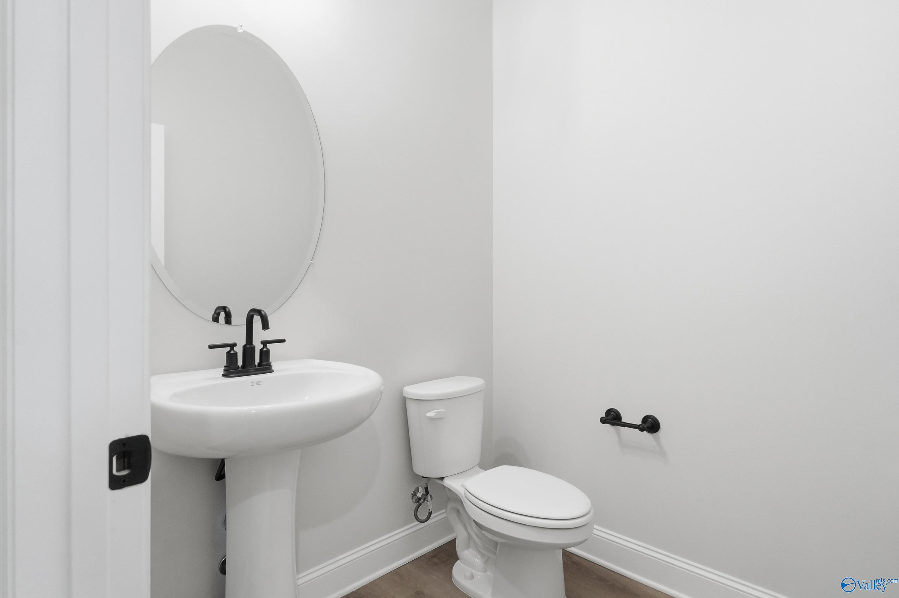 Bright powder room with white pedestal sink, round mirror, and toilet in Davidson Homes The Finleigh, Meridianville, Alabama