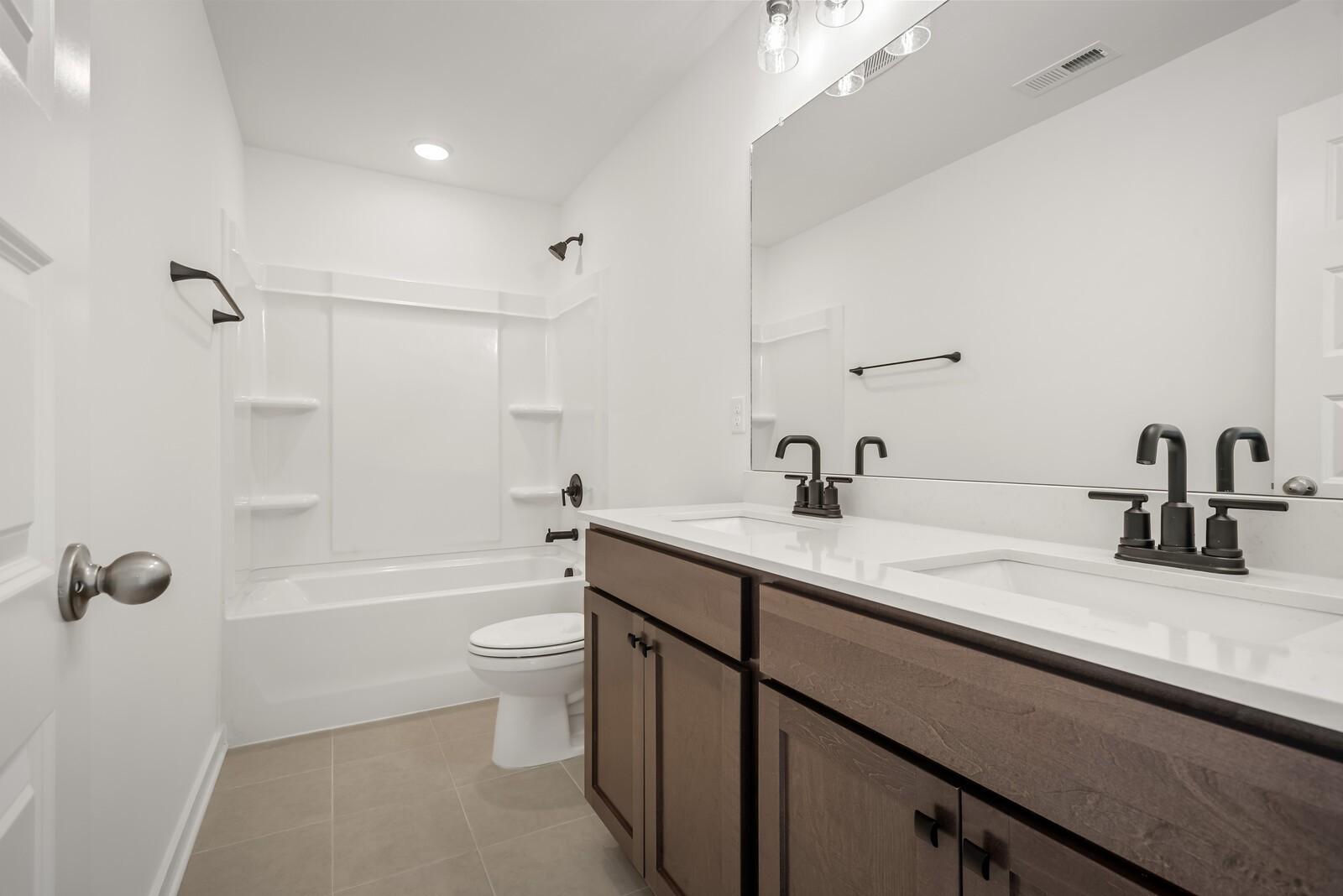 Elegant double vanity bathroom with soaking tub, black faucets, and tiled shower in Davidson Homes The Logan C, Gallatin, TN