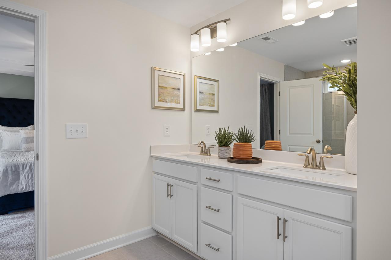 Modern primary bathroom with white double vanity, gold faucets, and potted plants at Gregory Village Townhomes in Lillington, NC by Davidson Homes