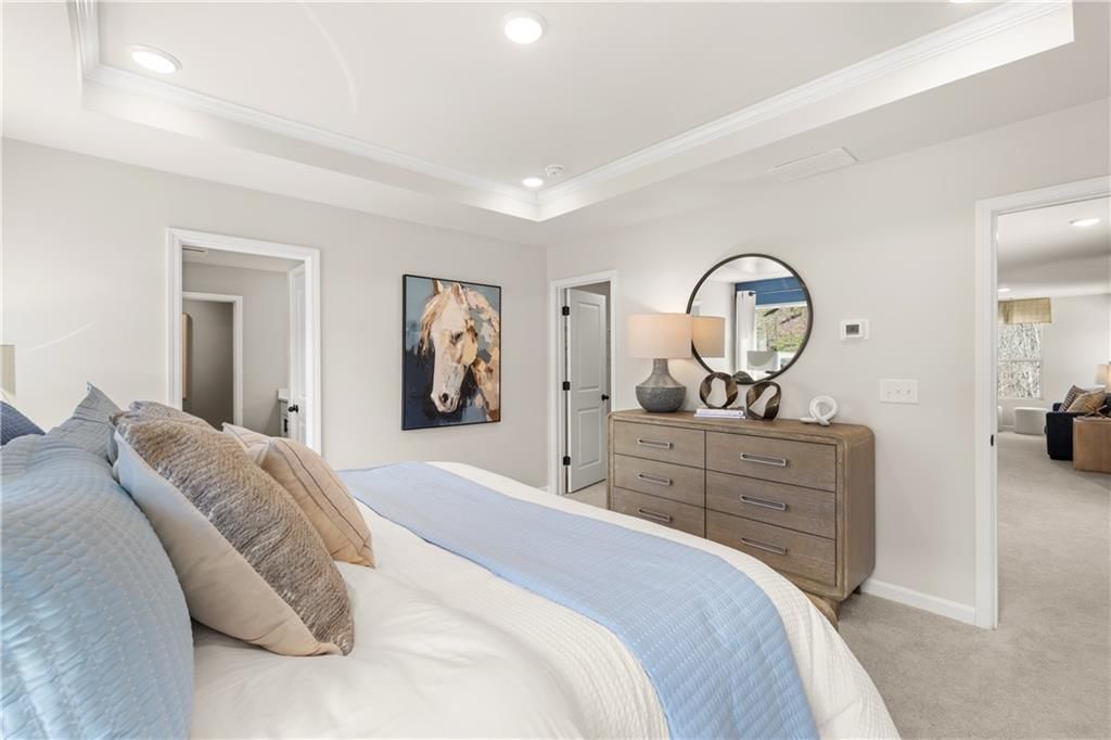 Elegant master bedroom with tray ceiling, wooden dresser, blue bedding, and horse artwork in Davidson Homes The Burton C, Canton, GA
