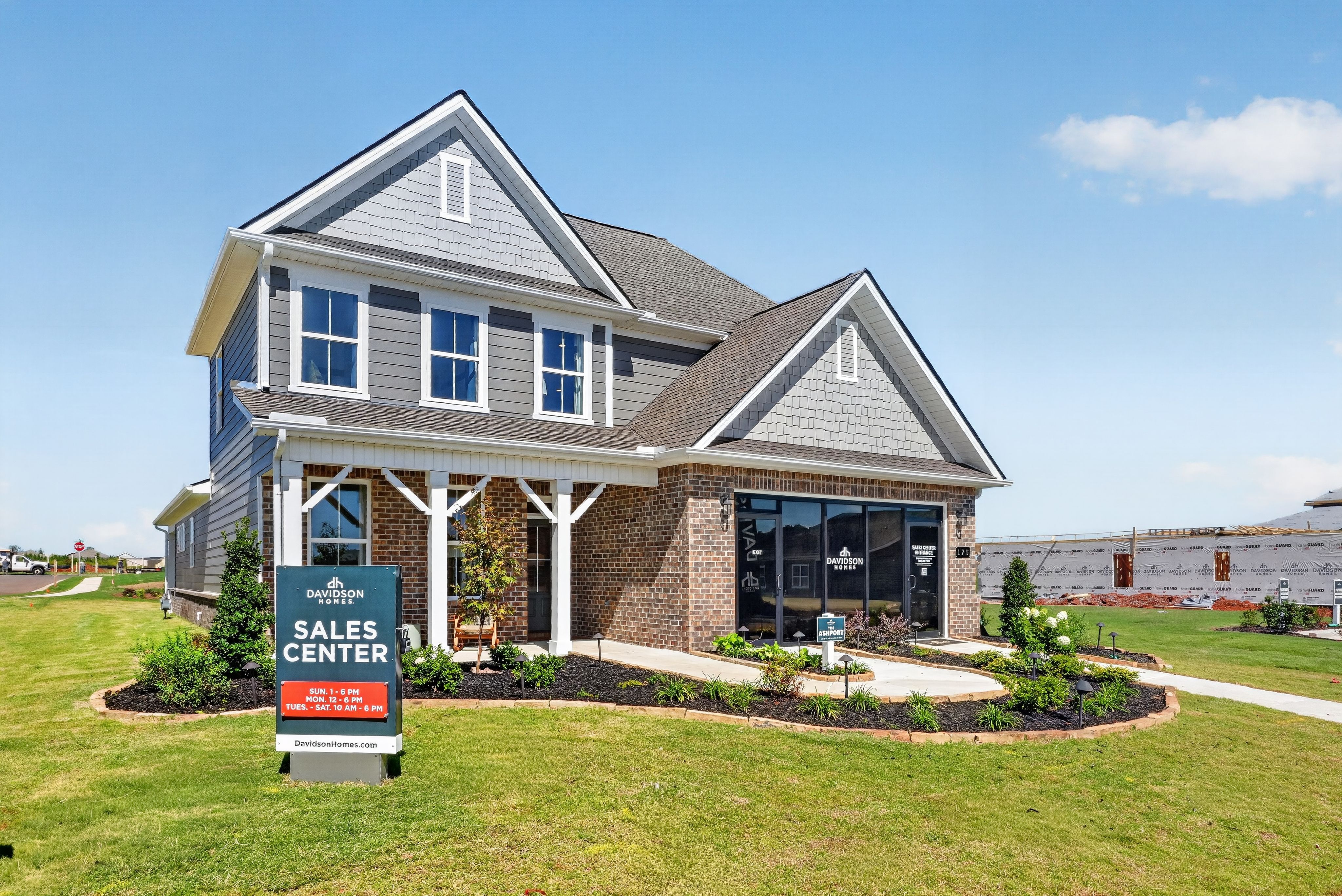 Davidson Homes sales center at Evergreen Mill in Madison, Alabama featuring gray siding, brick exterior, covered porch, and landscaped lawn