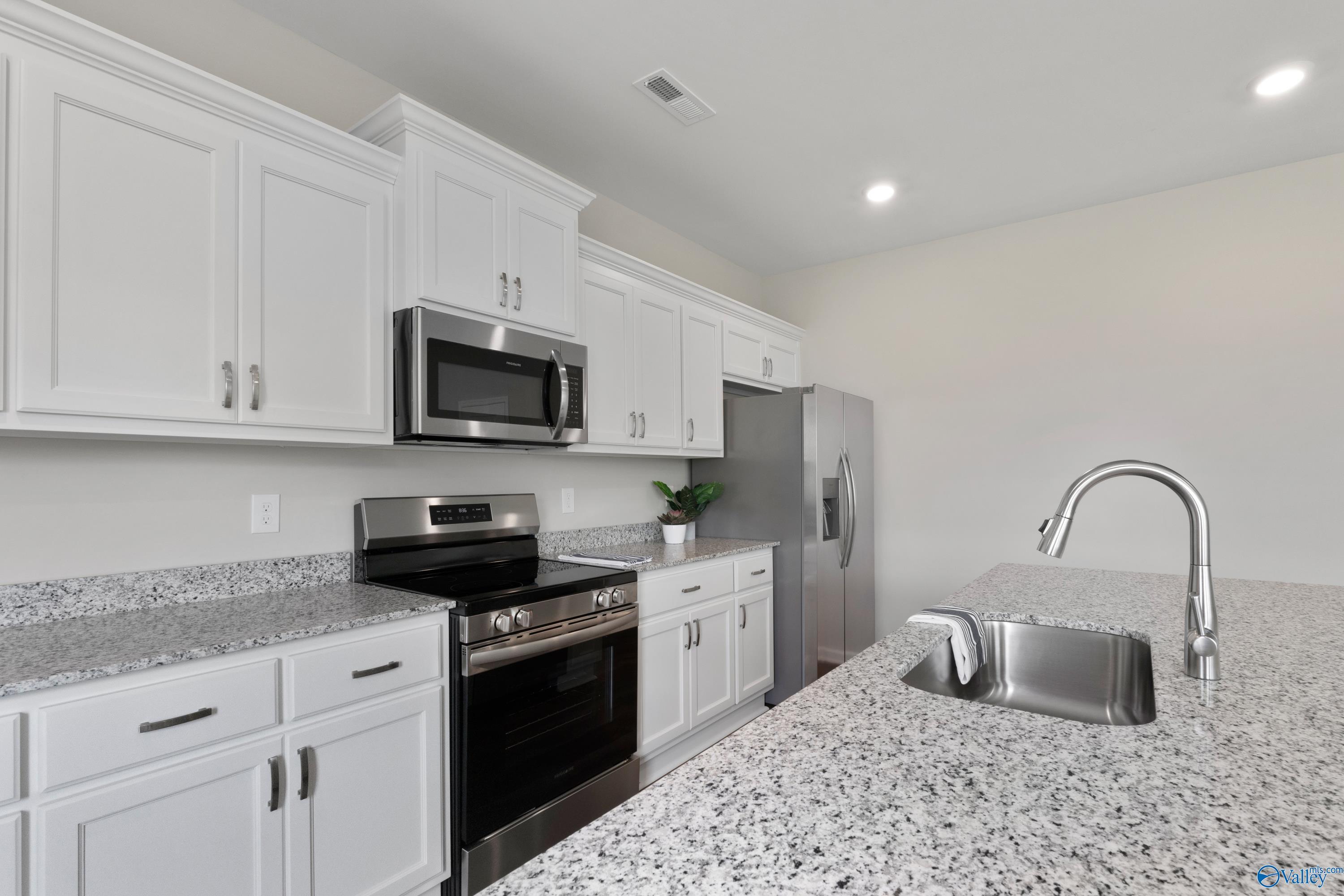 Modern white kitchen with granite countertops, stainless steel appliances in Davidson Homes The Noble, Madison, Alabama