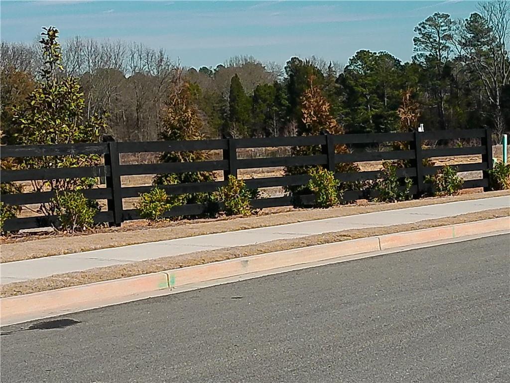 Black rail fence with evergreen shrubs and trees along sidewalk in Lake Shore, Winder, Georgia home community
