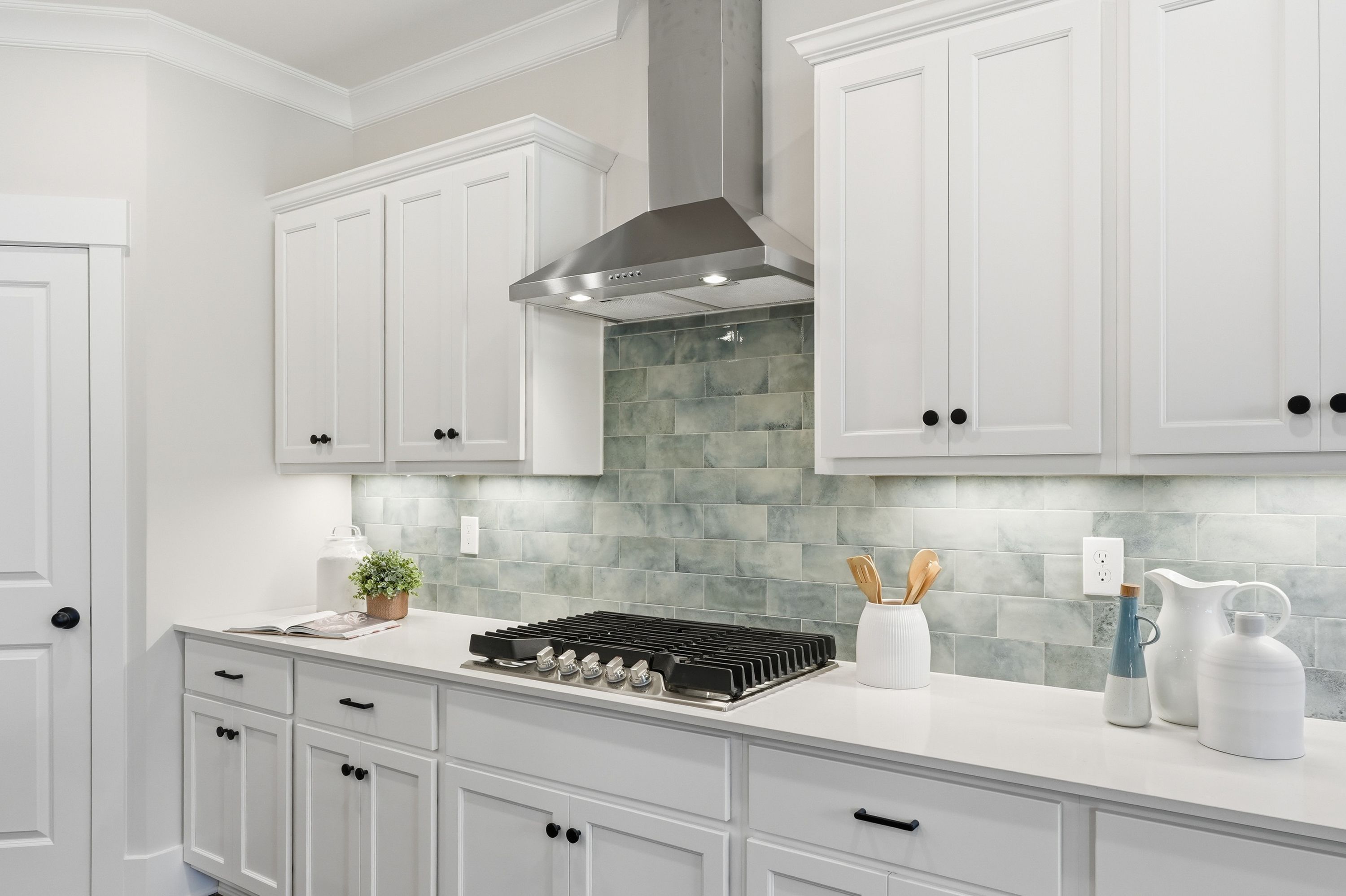 Modern white kitchen at Noble Ridge in Cullman Alabama with stainless steel range hood and teal subway tile backsplash