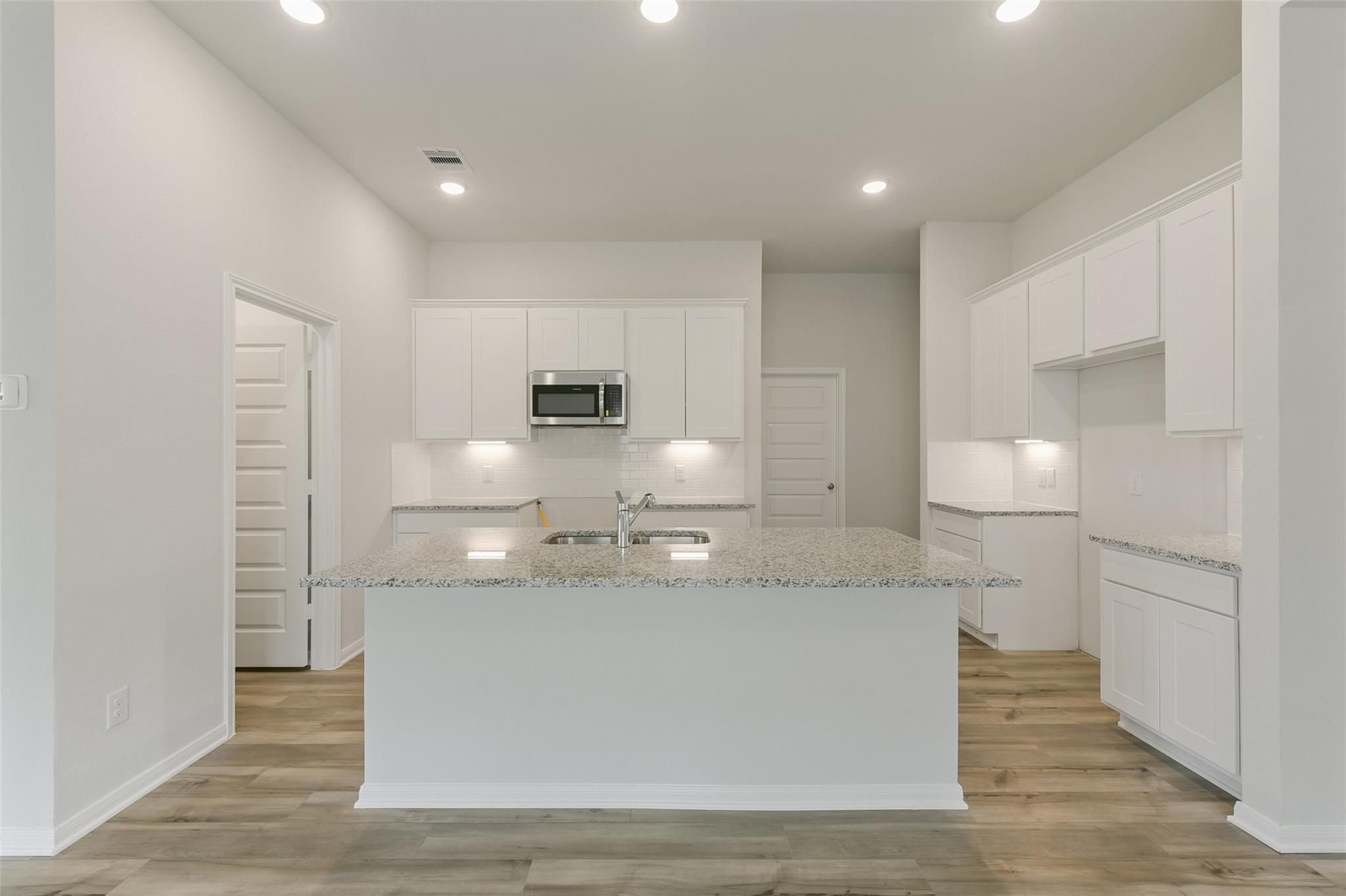 Modern white kitchen with granite island, stainless appliances, recessed lights in Davidson Homes The Laguna B, Dayton, Texas