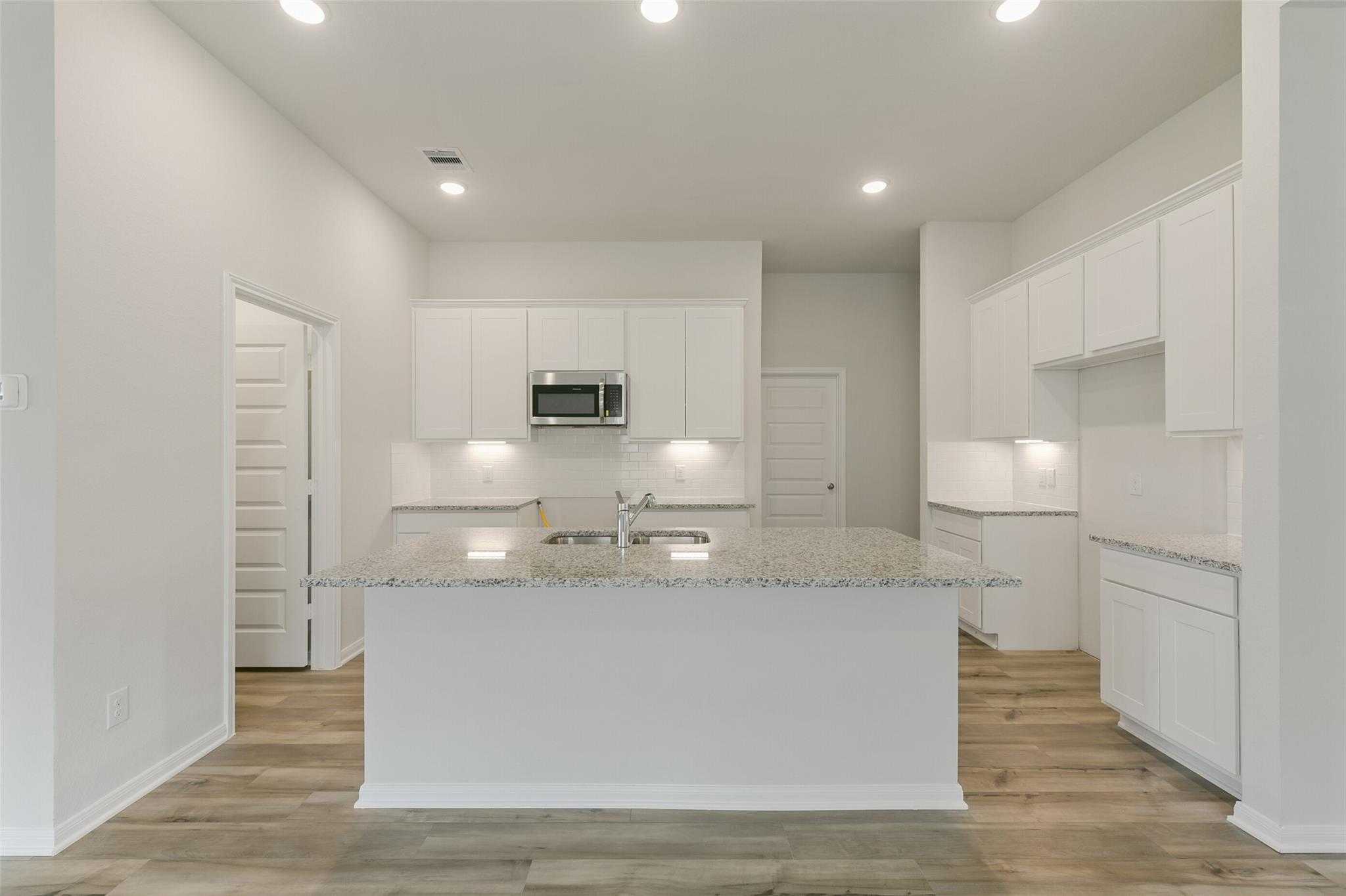 Modern white kitchen with granite island, stainless appliances, recessed lights in Davidson Homes The Laguna B, Dayton, Texas