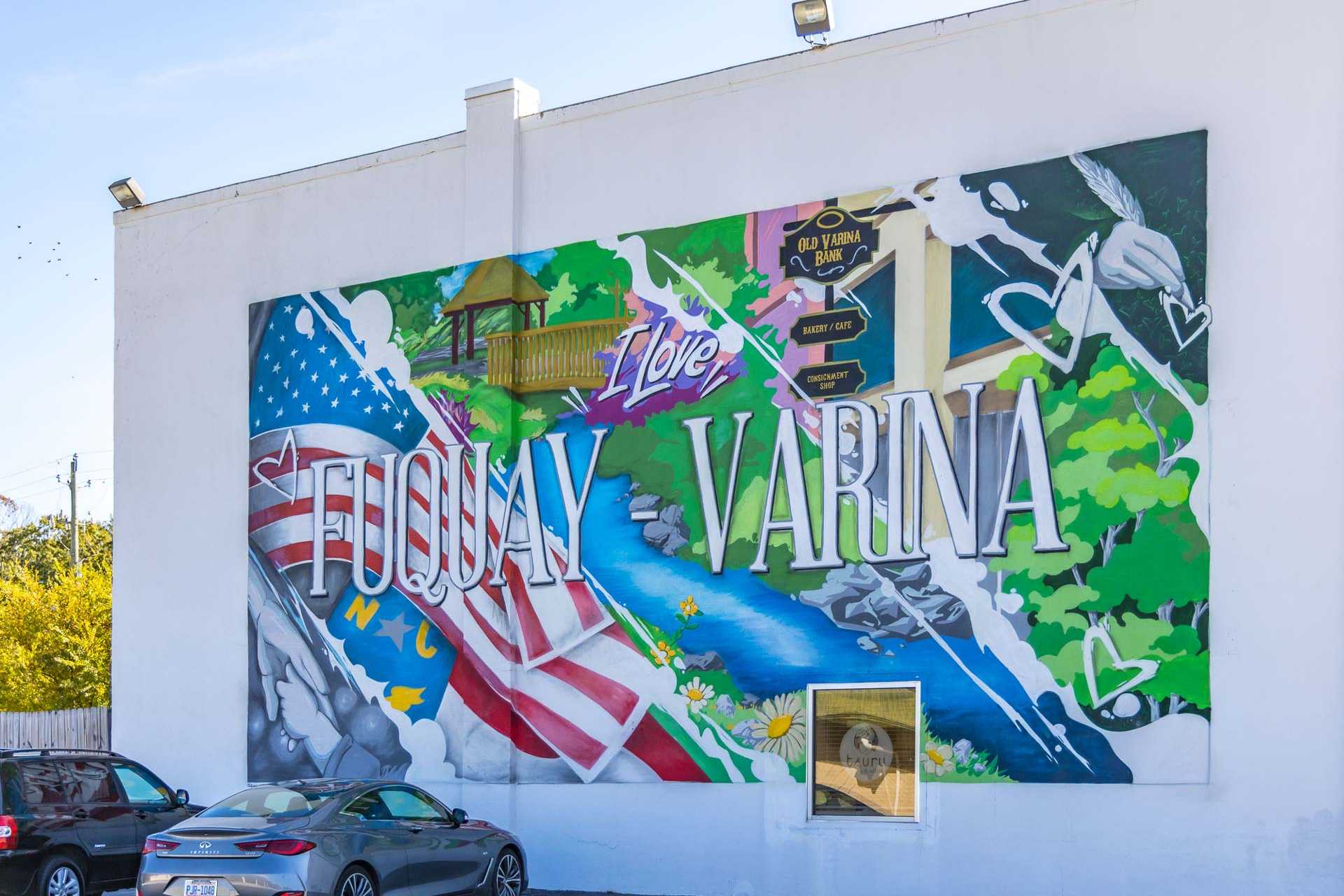 Vibrant "I Love Fuquay-Varina" mural on white wall with American flags, river scene, houses and greenery in Fuquay-Varina NC