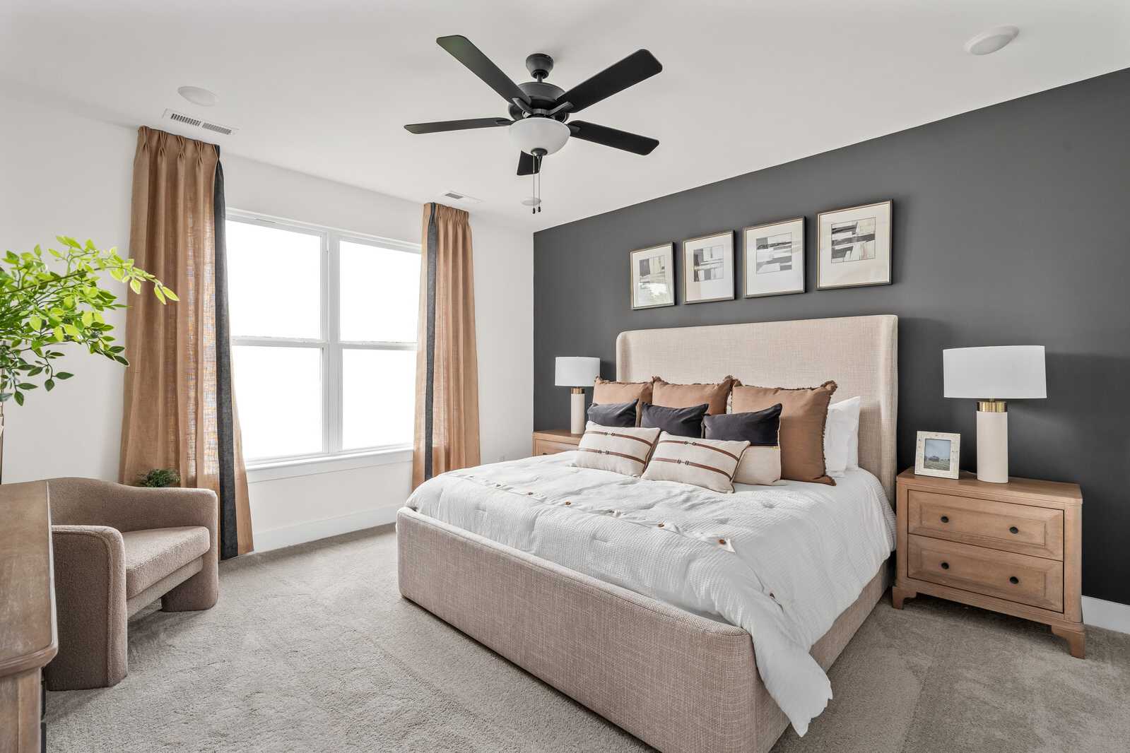 Spacious primary bedroom at Woods Crossing in Gallatin TN with beige king bed, gray accent wall, ceiling fans and large windows