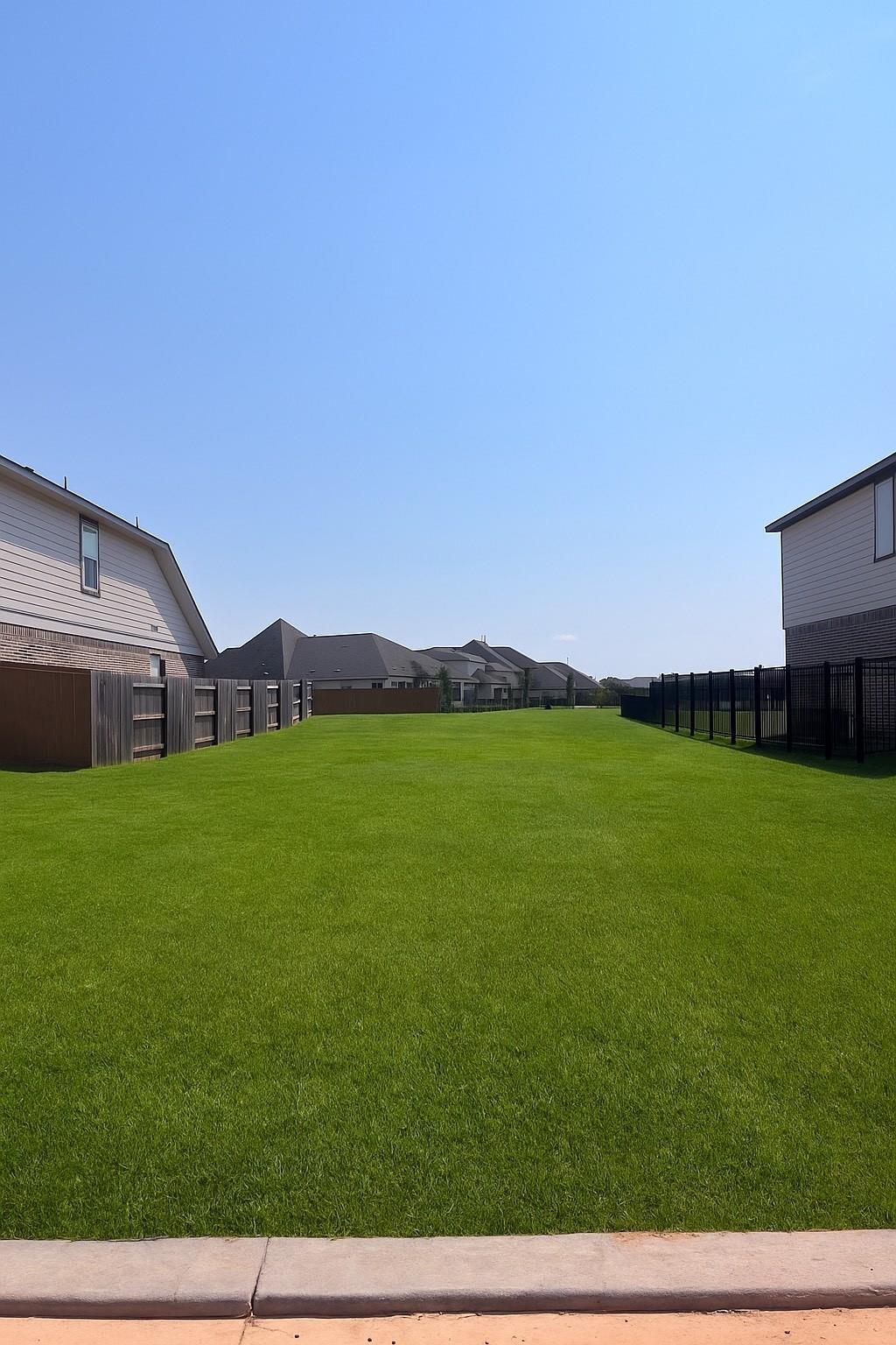 Expansive green lawn with black fencing and neighboring homes under blue sky in Robins Landing, Houston, Texas Davidson Homes The Comal F