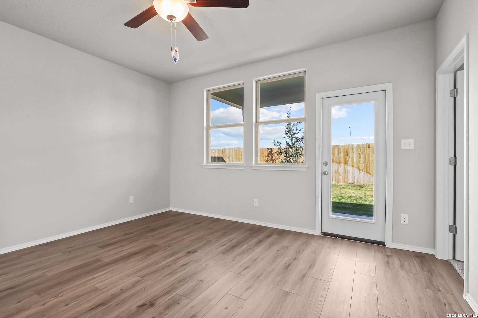Bright living room with gray walls, wood floors, ceiling fan, large windows, and sliding door to fenced backyard in Davidson Homes The Frio B, San Antonio