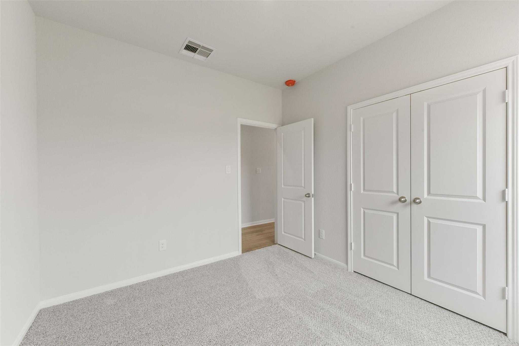 Spacious bedroom with gray carpet, white walls, double closet doors in Davidson Homes The Laguna B, Magnolia, Texas