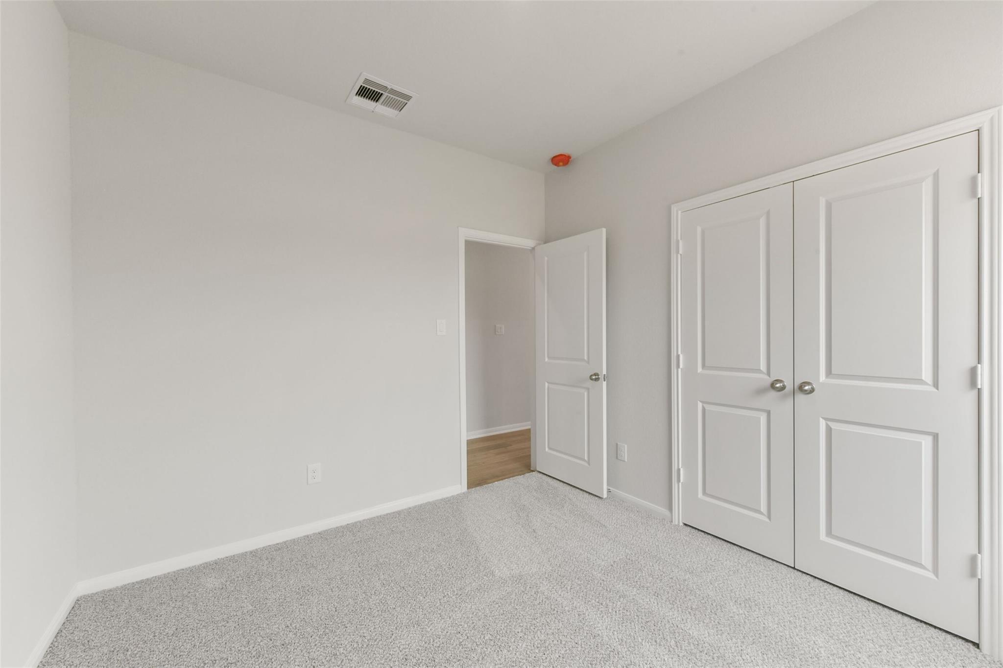 Spacious bedroom with gray carpet, white walls, double closet doors in Davidson Homes The Laguna B, Magnolia, Texas