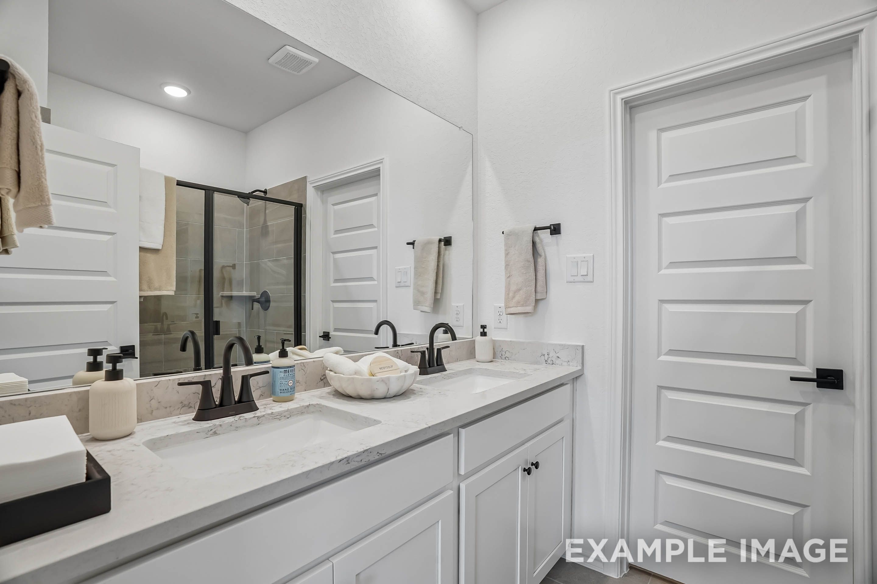 Modern master bathroom in The Pinecrest featuring dual vanities, marble countertops, and a walk-in glass shower.