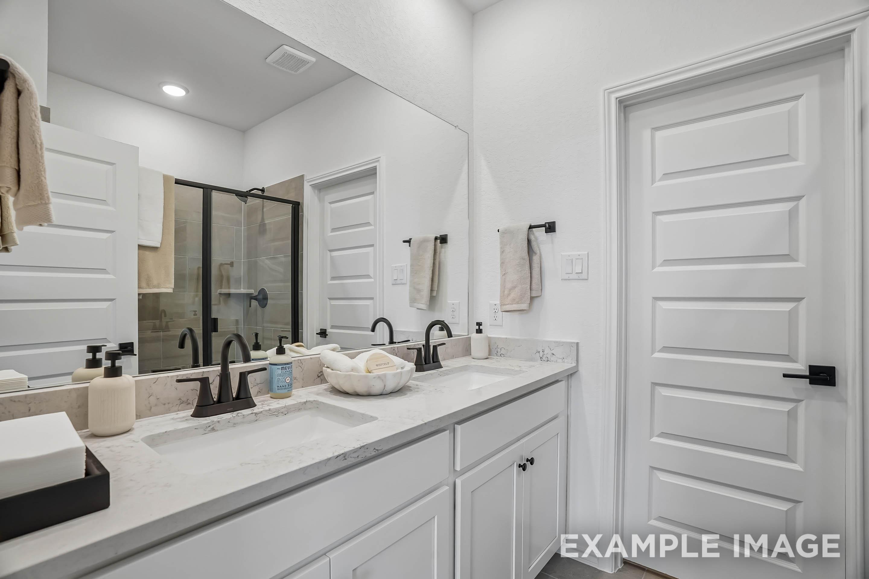 Modern master bathroom in The Pinecrest featuring dual vanities, marble countertops, and a walk-in glass shower.