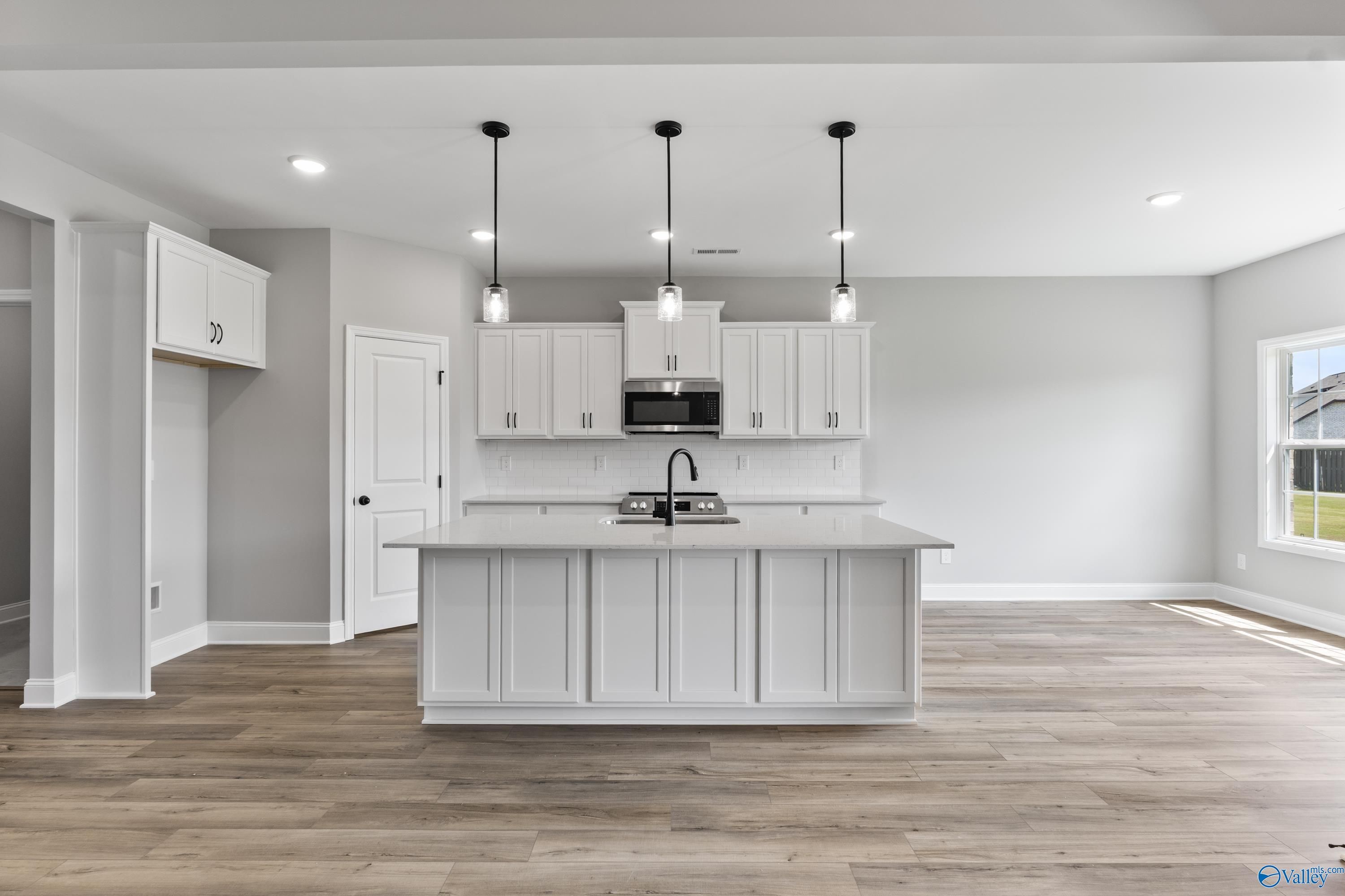 Modern white shaker kitchen with large island, pendant lights, and hardwood floors in Davidson Homes The Montgomery B With Bonus, Toney, AL