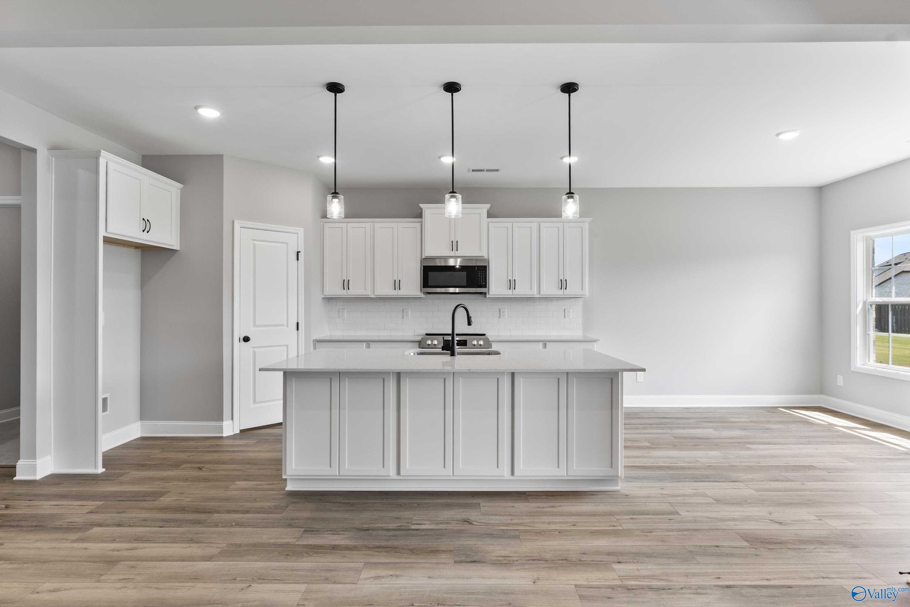 Modern white shaker kitchen with large island, pendant lights, and hardwood floors in Davidson Homes The Montgomery B With Bonus, Toney, AL