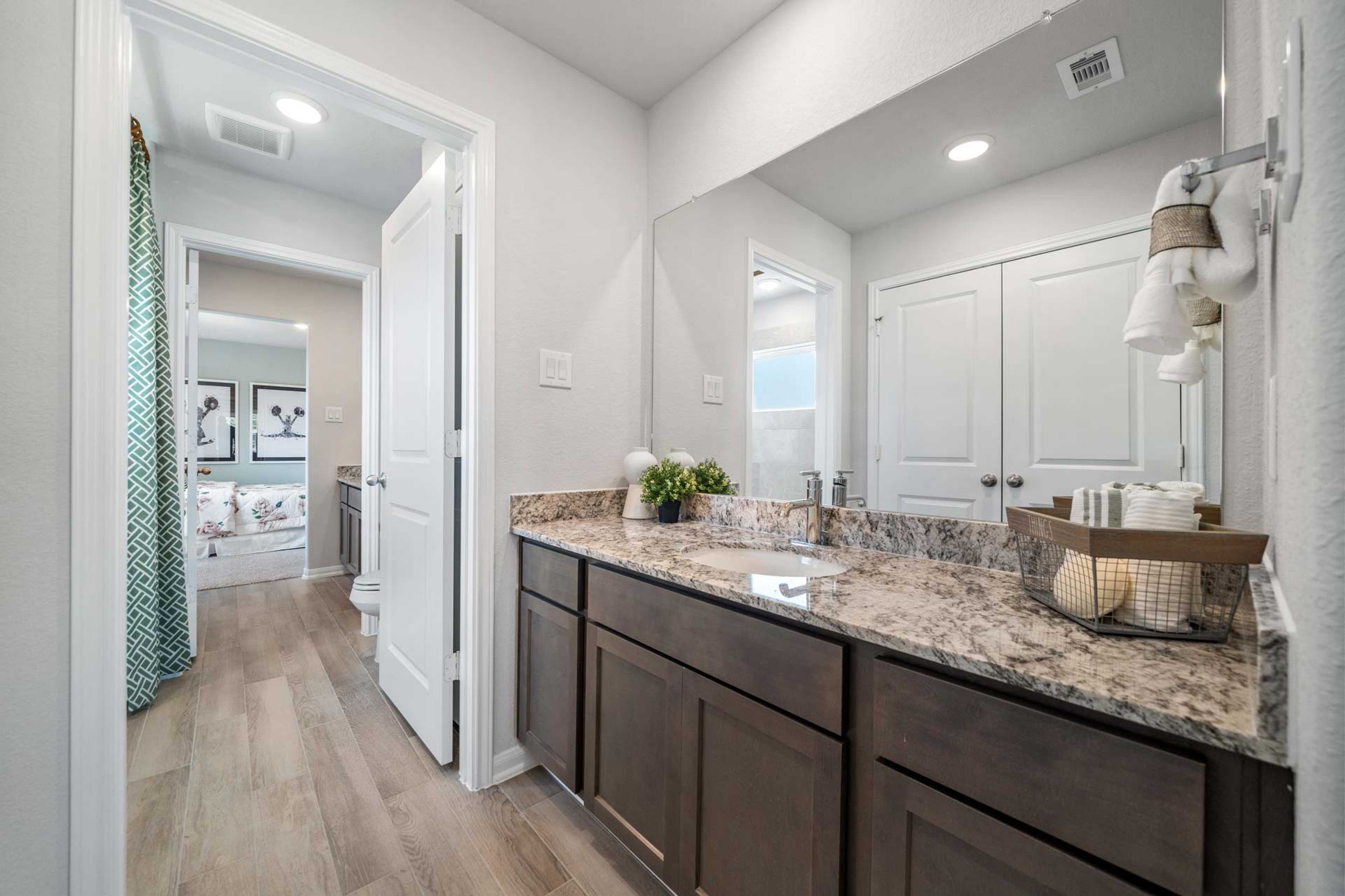 Modern primary bathroom at Windmill Estates in Magnolia TX with double vanity, granite counters, and hardwood floors