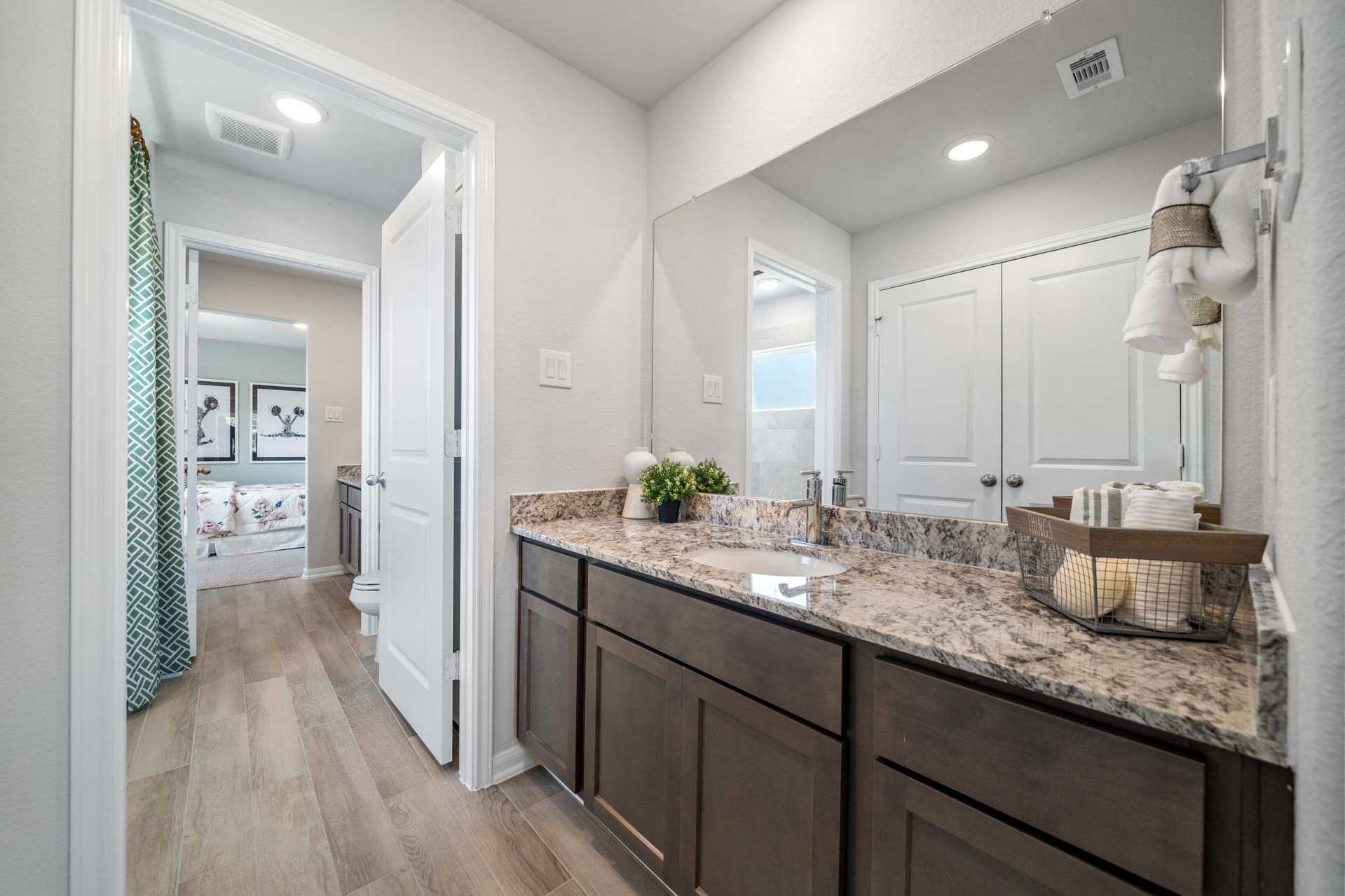 Spacious primary bathroom at Windmill Estates in Magnolia Texas featuring double vanity with granite counters and hardwood floors